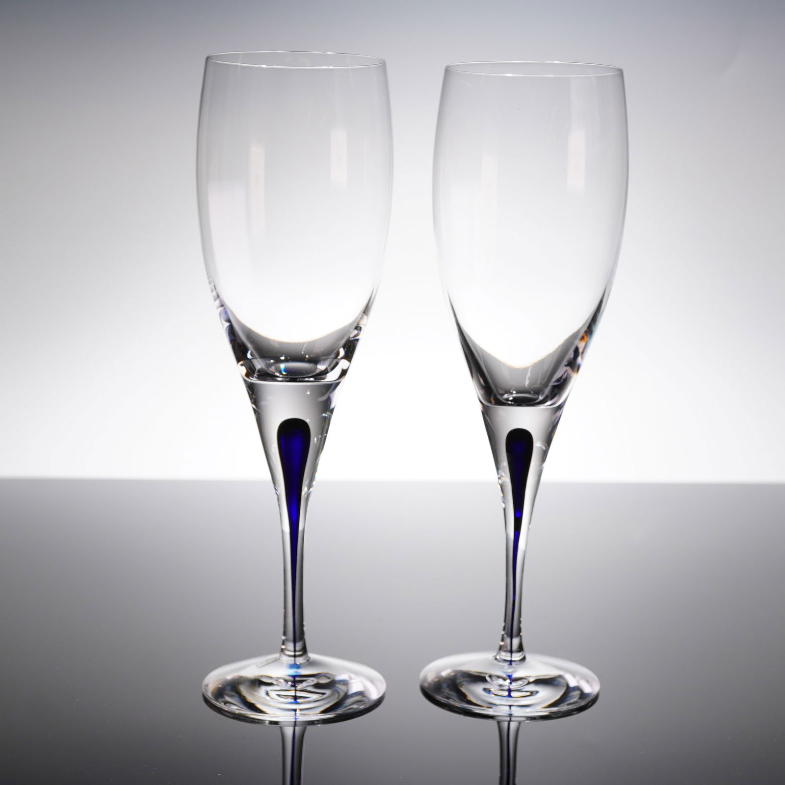 A Pair of Orrefors Intermezzo Blue Crystal Champagne Flutes: A pair of contemporary crystal champagne fi?utes from the Orrefors Intermezzo Blue collection. Each fi?ute features a clear, slender bowl atop a substantial solid glass stem and circular foot. The