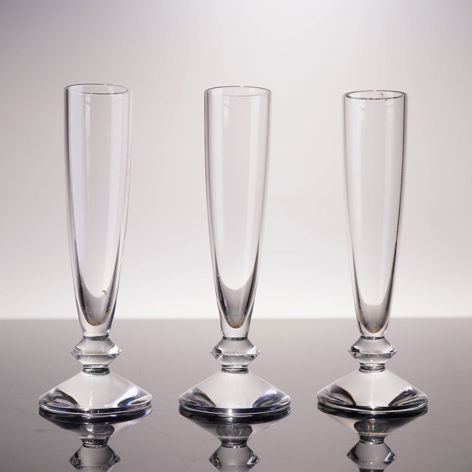 Three Baccarat Vega Vodka Glasses: Three Baccarat 'Vega' vodka glasses. Each crafted from high-quality clear crystal, featuring a tall, slender bowl, a faceted stem, and a circular foot. The underside of each foot is marked with an