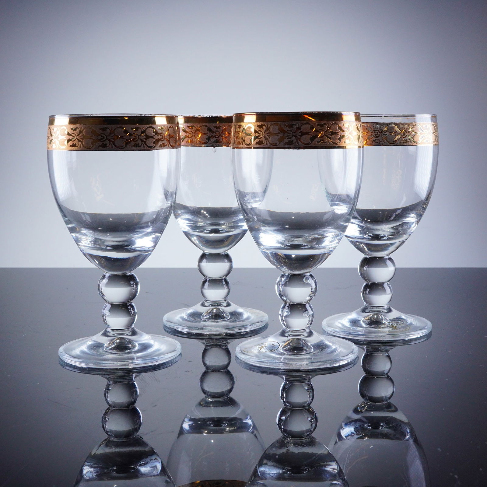 4pc J Preziosi Italian Gold Rim Wine Glasses: A collection of four stemmed glasses by J Preziosi. These clear glasses feature a tapered bowl supported by a double-knop stem and a wide, circular foot. The primary decoration is a broad gold-colored