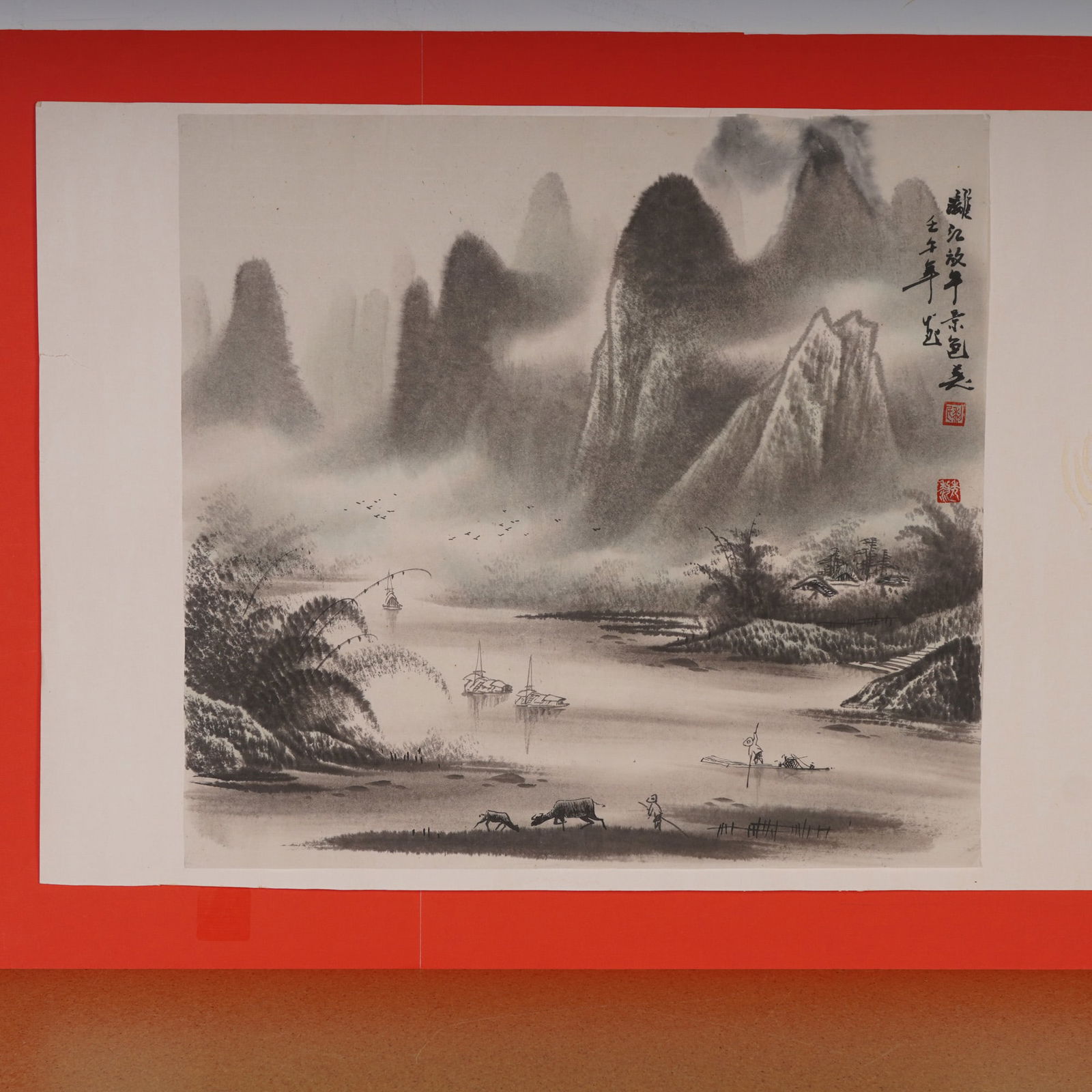 Chinese Ink on Paper Landscape Painting: A finely rendered Chinese ink painting depicting a serene landscape scene, executed on a thin gray-toned paper mounted to a white backing and set against a red paper board. The composition features an