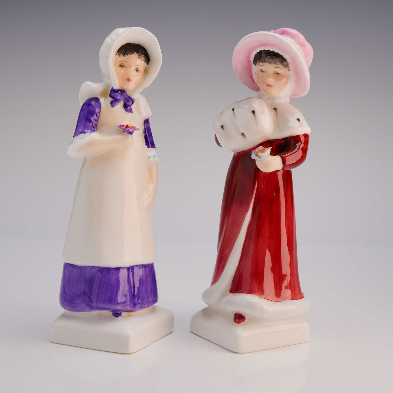 2pc Royal Doulton Figurines Anna HN2802 and Sophie HN2833: Both figures depict young women in period costume, finished in high-gloss polychrome glazes and mounted on square white bases. Anna (HN 2802, copyrighted 1975) is dressed in a purple and white apron d