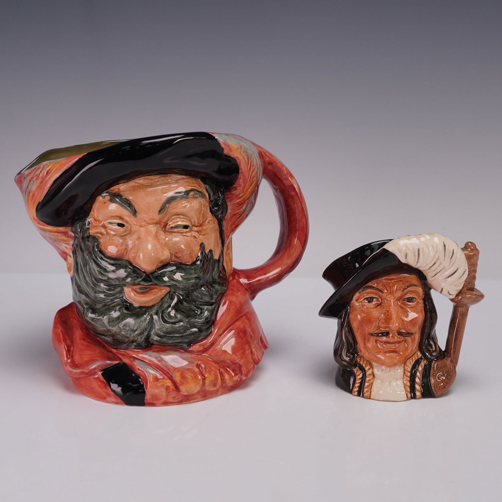 2pc Royal Doulton Character Jugs, Falstaff D6287 & Athos D6452: This lot offers two Royal Doulton character jugs, featuring Falstaff D6287 (large size) and Athos D6452 (small size). Falstaff, the jovial Shakespearean knight, is depicted with a broad grin, flowing