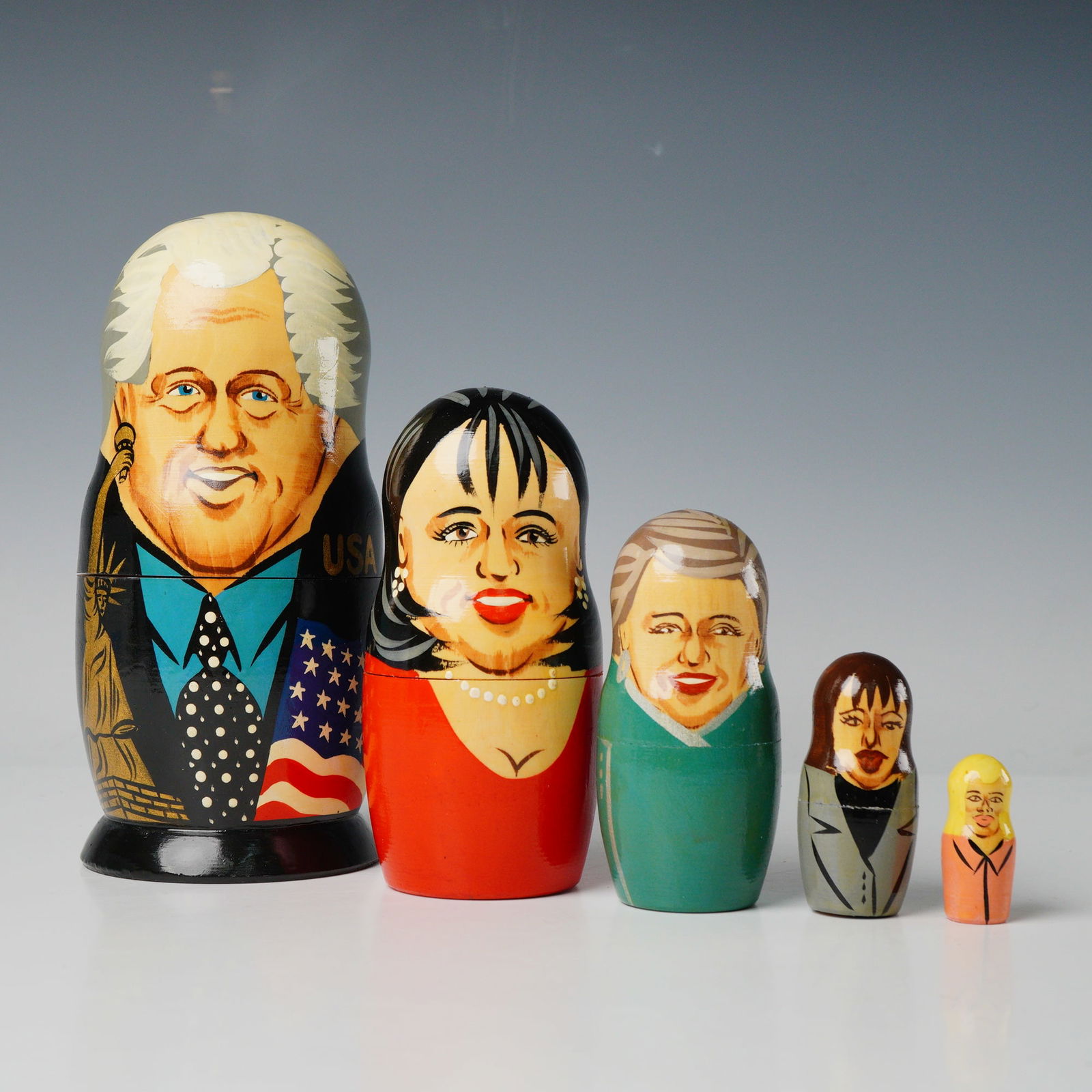 5 Political Satire Matryoshka Dolls Bill Clinton & Associates: A set of five hand-painted wooden Matryoshka nesting dolls depicting political caricature subjects. The largest doll features Bill Clinton, dressed in a suit with the Statue of Liberty, the American