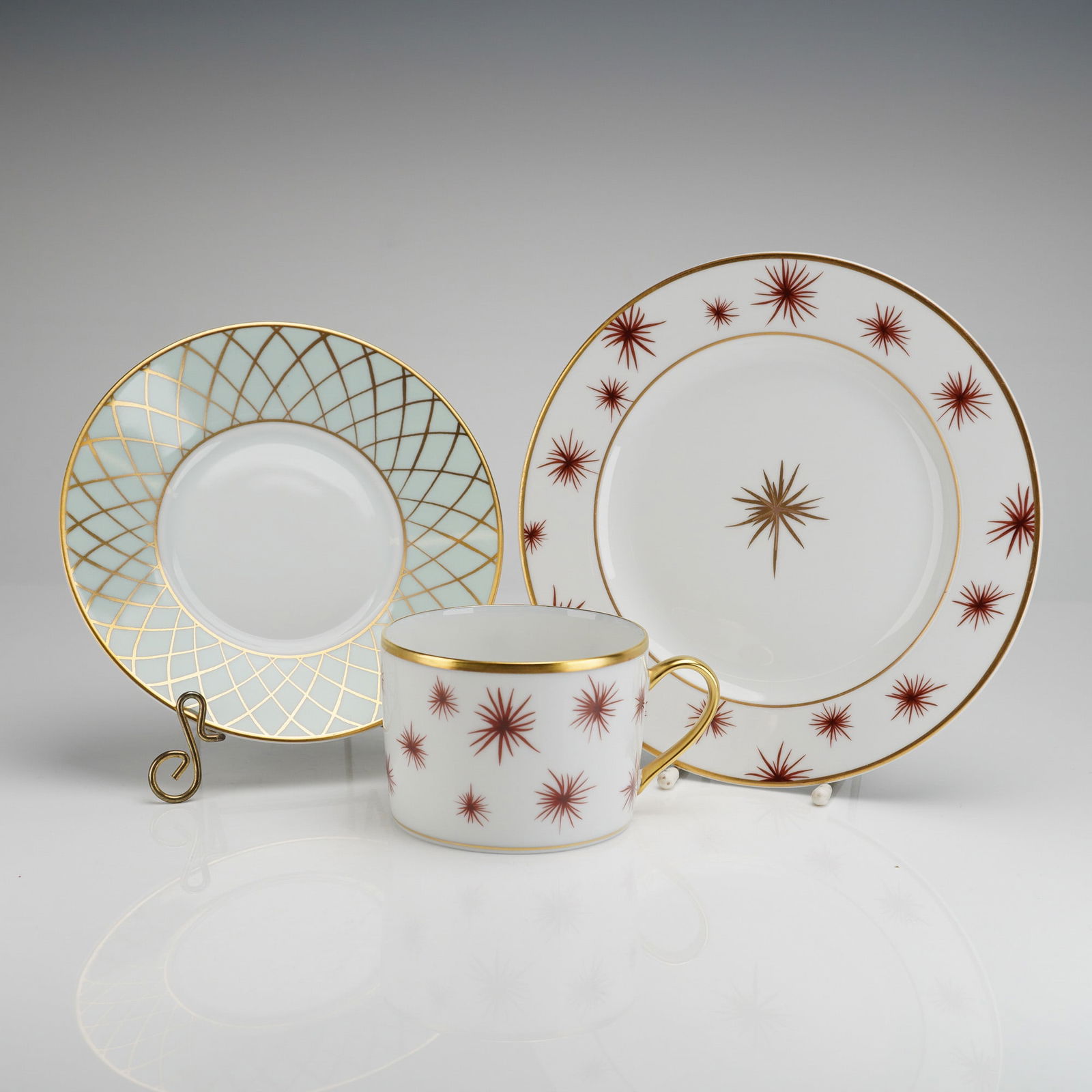 A Trio of Bernardaud Limoges Porcelain Tableware in the etoile Pattern: A three piece set of Bernardaud Limoges porcelain tableware in the Etoile pattern, consistent with Mid-Century Modern design aesthetics. The set comprises a flat cup, a saucer, and a bread and butter