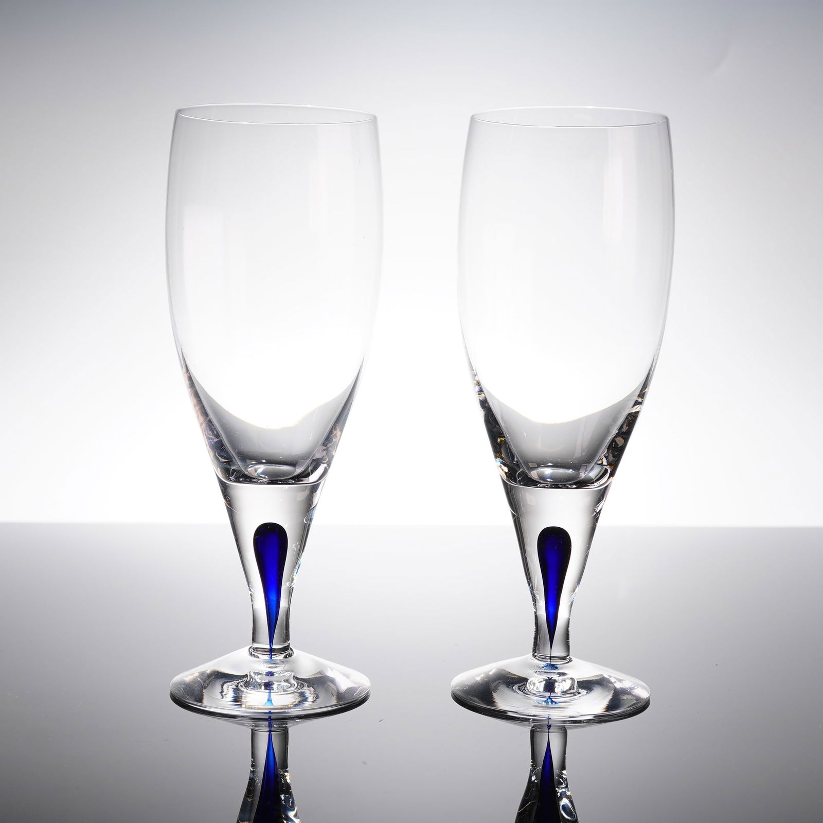 2 Orrefors Intermezzo Blue Champagne Flutes Lagerbielke: A pair of Orrefors Intermezzo Blue champagne flutes, designed by Erika Lagerbielke. These glasses are constructed from clear colorless crystal glass in a modern style, featuring tall, slightly tapered