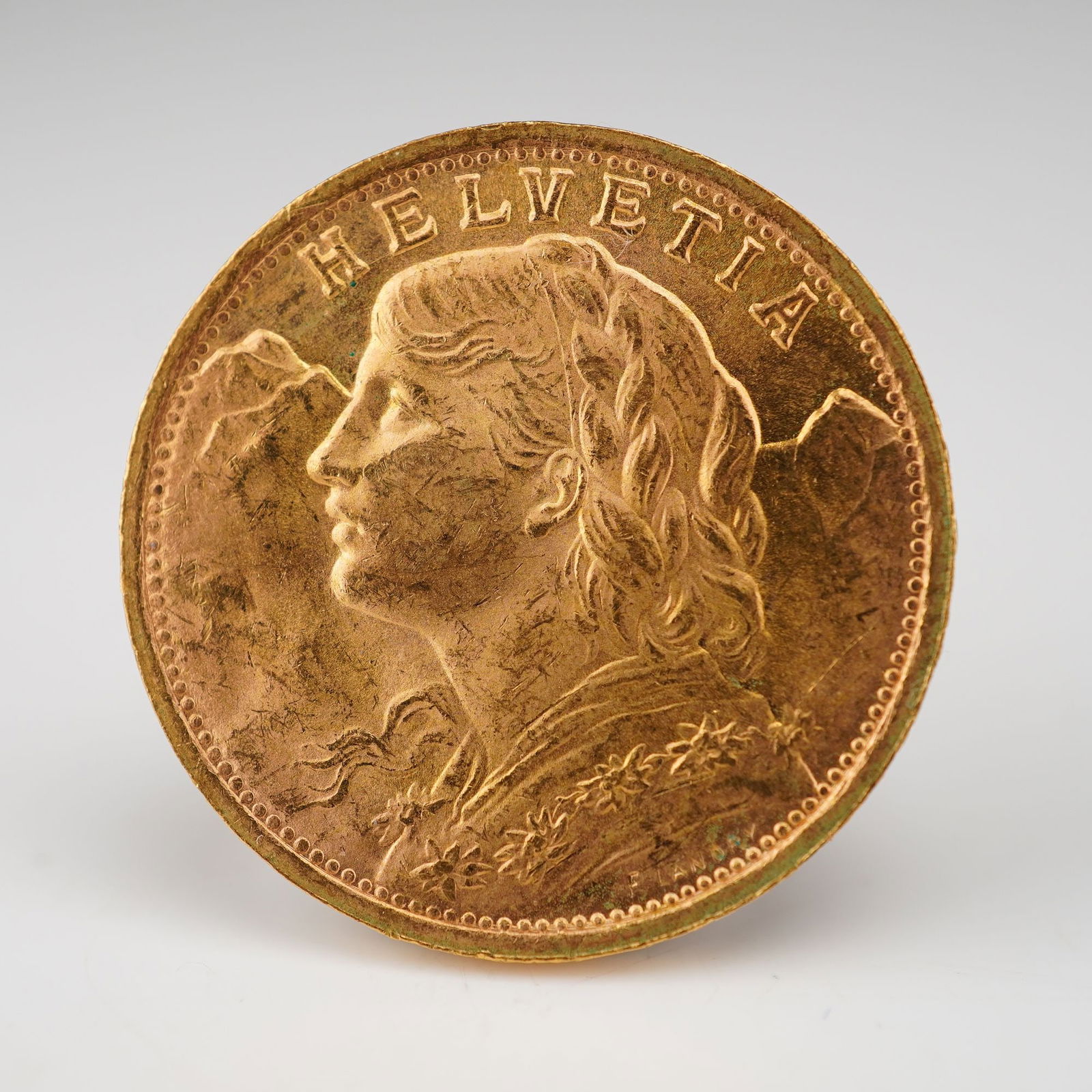 1947-B 20 Francs Swiss Vreneli Helvetia Gold Coin: Bern Mint in Switzerland. Featuring 7 embossed stars and "AD LEGEM ANNI MCMXXXI" along the edge. The obverse presents a left-facing bust of a young woman from Oberhasli, adorned with flowing tresses a
