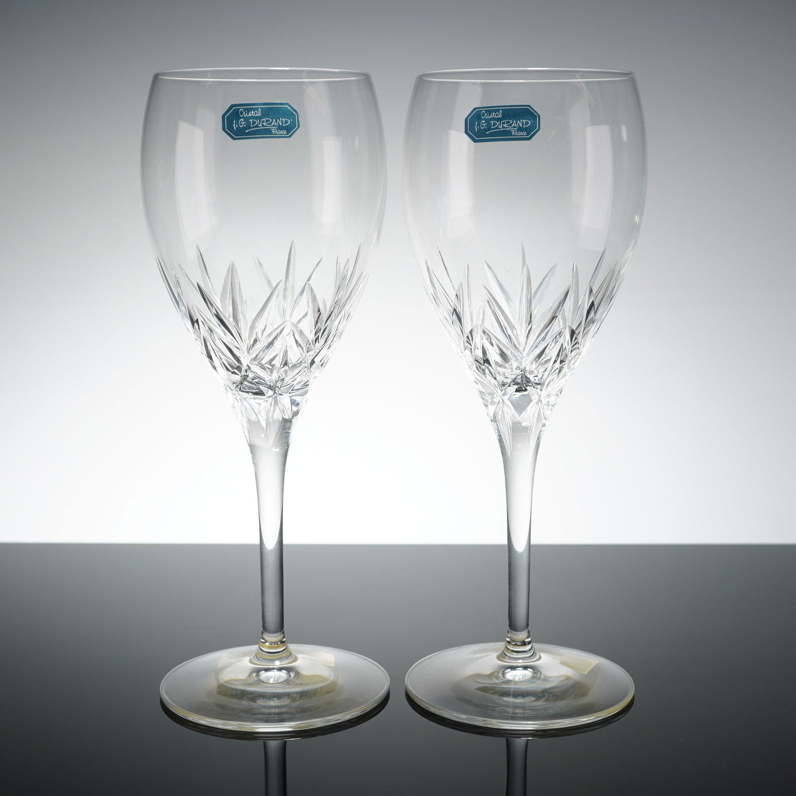 Pair of J.G. Durand France Crystal Wine Glasses, Orion: Each glass features a clear, tapering bowl decorated with an intricate starburst cut pattern on the lower half, supported by a slender, plain stem and a circular foot. The items are constructed of 24