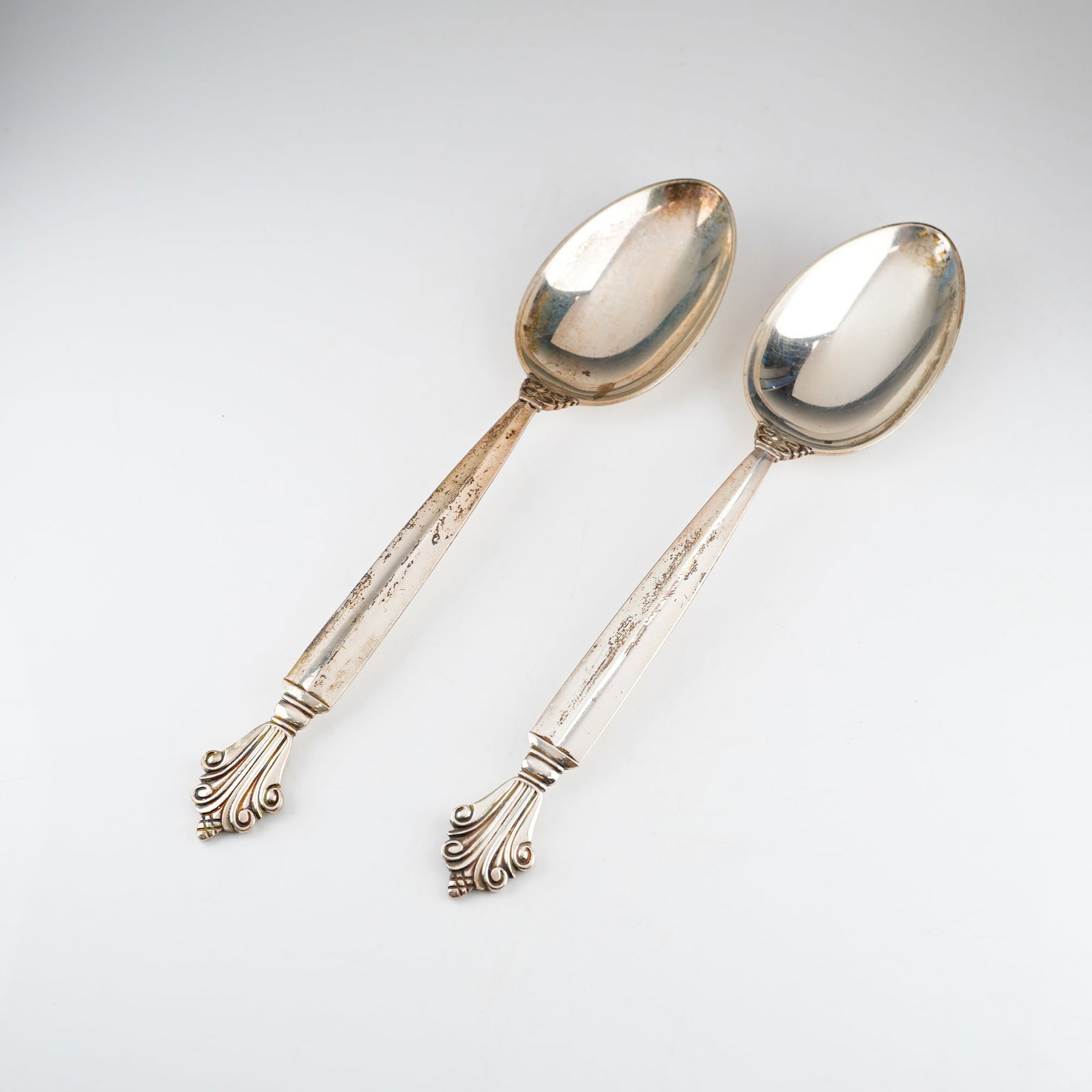 2pc of Georg Jensen Sterling Silver Spoons, Acanthus: A pair of sterling silver spoons in the Acanthus pattern, designed by Johan Rohde for Georg Jensen. The items feature tapered handles terminating in stylized acanthus leaf and scroll motifs, emblemati