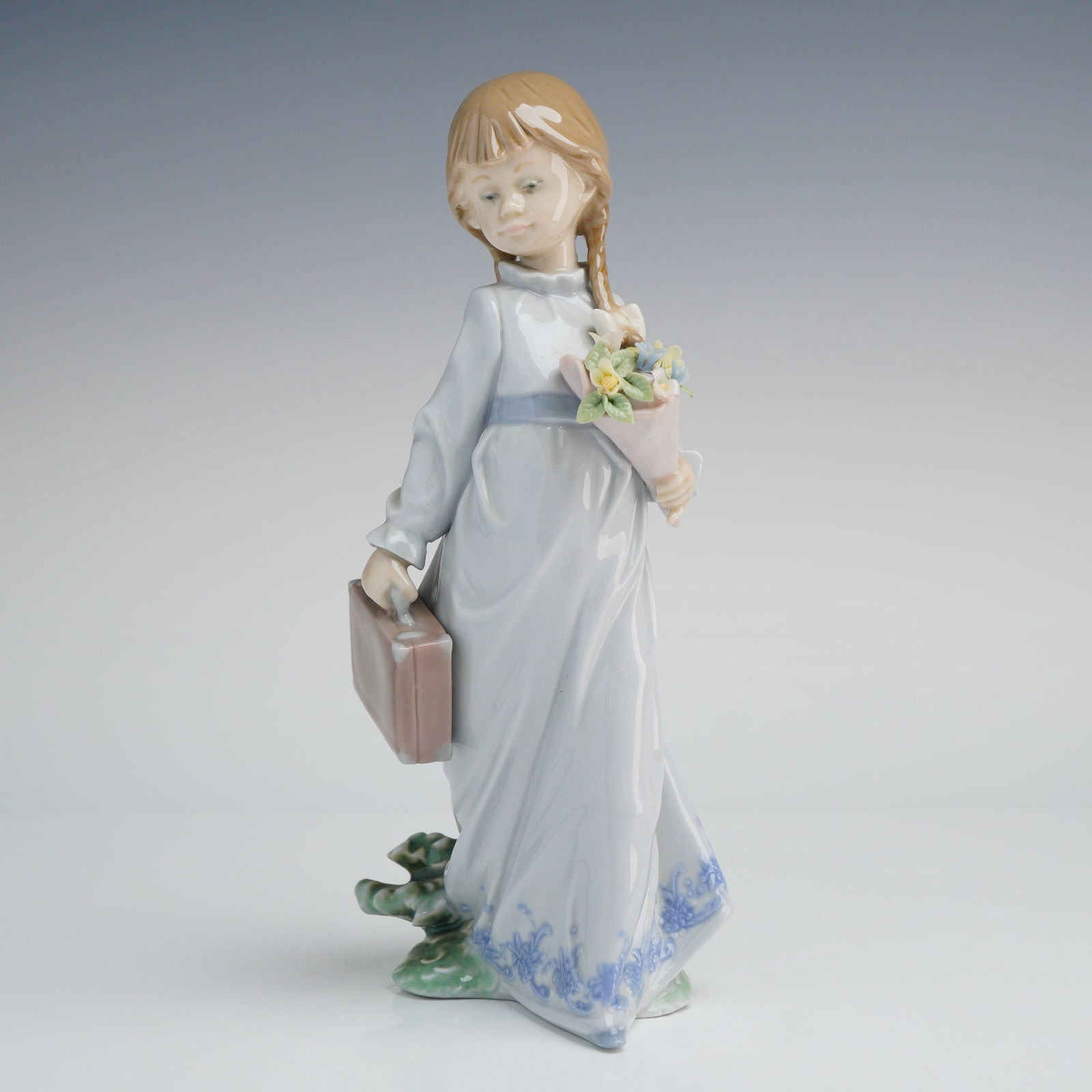 Lladro School Days Figurine 7604 with Box: A glazed porcelain figurine by Lladro, model number 7604, titled "School Days." The figurine depicts a young girl with light brown braided hair, wearing a long white gown accented by a blue sash and b