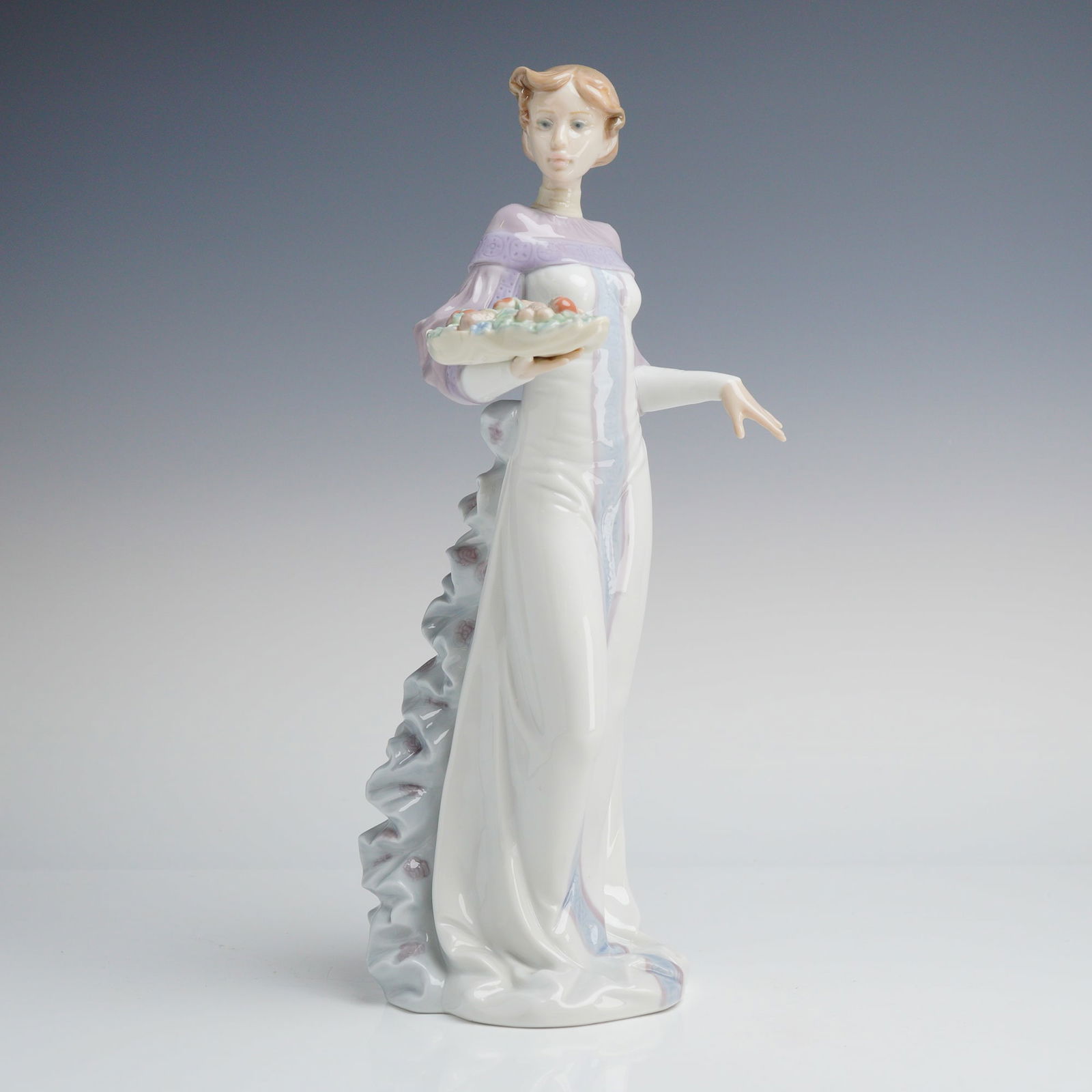 Lladro Winter Love Premiere Issue Porcelain Figurine 6621: A Lladro Porcelain Sculpture, Winter Love (01006621), depicting a woman in a white and lavender gown holding a basket, marked "LLADRO," "DAISA 1998," and "1999 PREMIERE ISSUE," presented in its origin