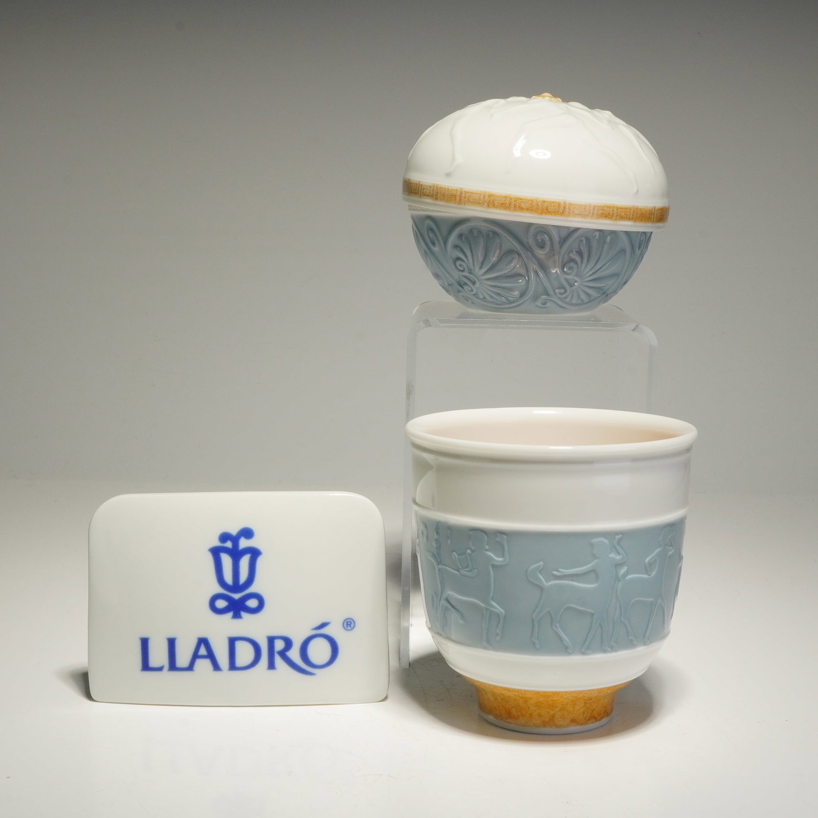 3pc Lladro Porcelain Cup Candle Holder, Lidded Jewelry Box, and Plaque: A collection of Lladro pieces including a lidded jewelry box, cup candle holder, and name plaque. The candle holder features bas-relief centaurs on a pale blue ground, a footed base with a mottled bei