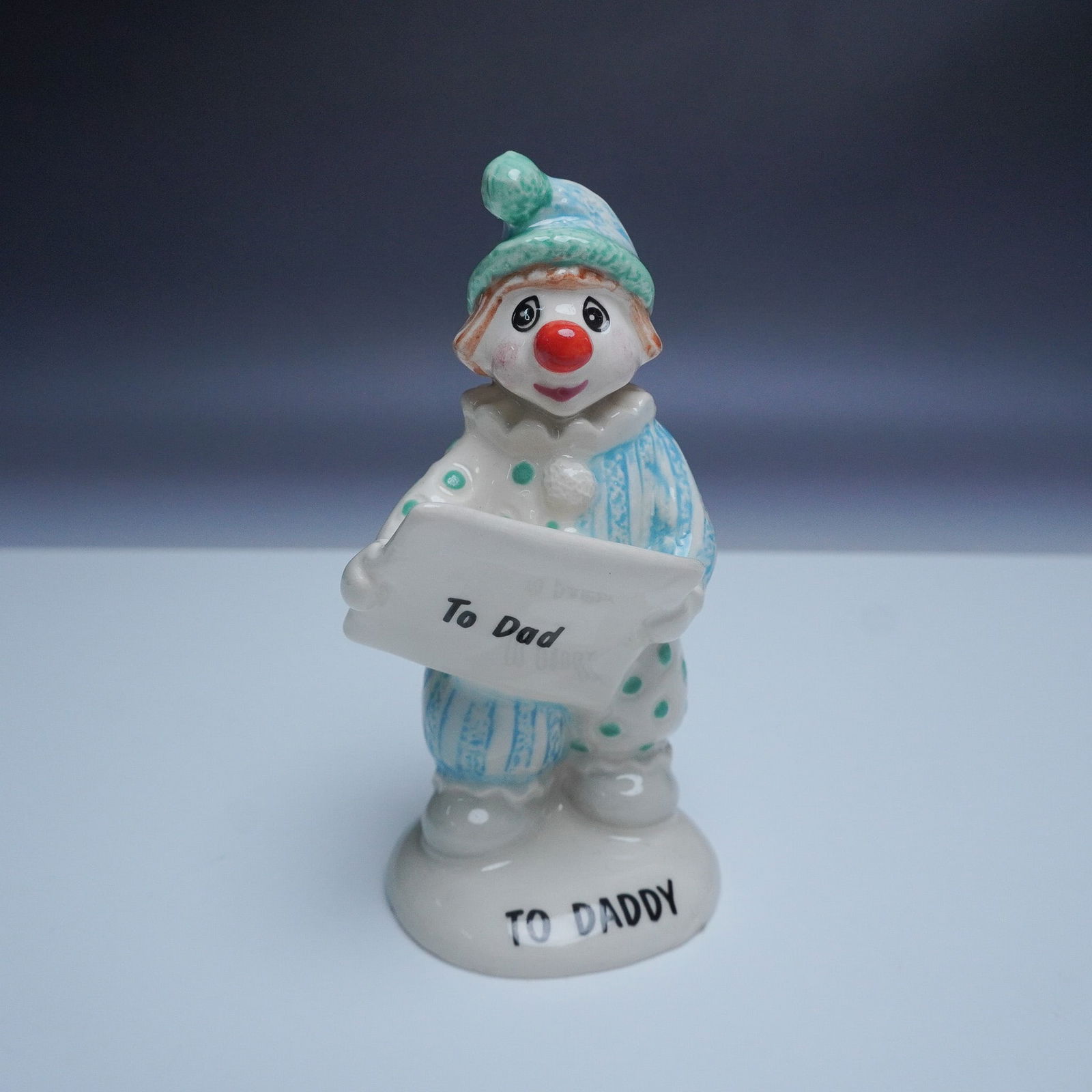 Beswick To Daddy Clown Figurine: This charming John Beswick handmade ceramic figurine, titled To Daddy, features an adorable clown dressed in a blue and white outfit, holding a sign that reads To Dad. The base of the figurine is insc