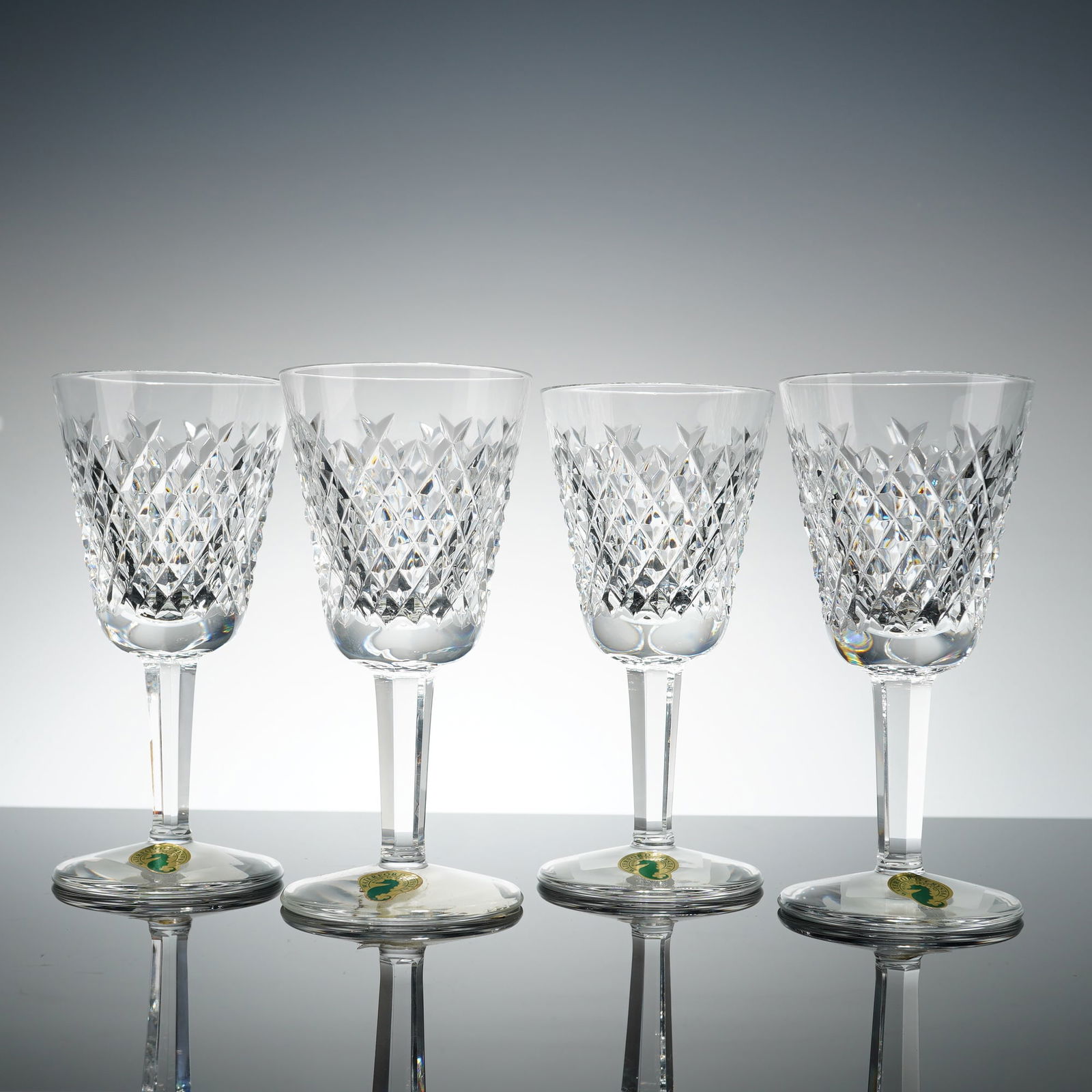 Set of 4 Waterford Crystal White Wine Glasses, Alana: Each glass features a hand-cut diamond and wedge pattern on the bowl, supported by a multi-faceted hexagonal stem and a circular foot. The items bear the manufacturer's acid-etched mark on the base, a