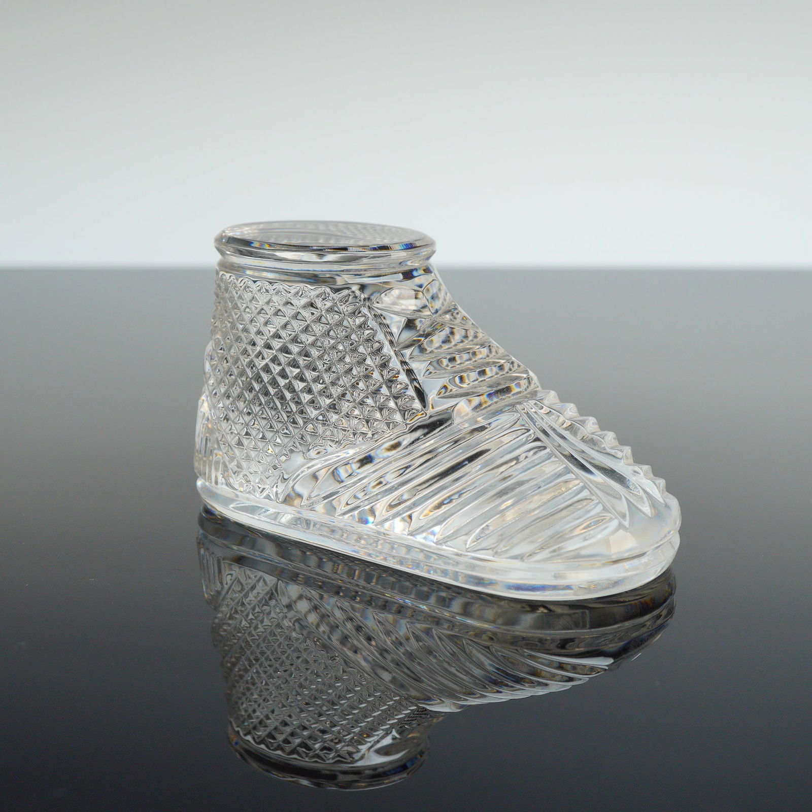 Waterford Crystal Baby Bootie Paperweight: A Waterford crystal baby boot paperweight crafted from clear lead crystal. The figurine is designed in the form of a baby bootie featuring detailed diamond-cut patterns on the sides and linear ribbing