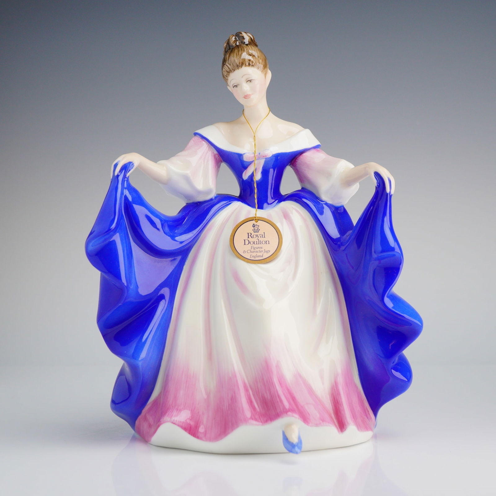Royal Doulton Colorway Figurine, Sara HN3308: The piece was modeled by Peggy Davies and depicts a young woman in a voluminous period gown. The figurine features a glossy cobalt blue overskirt and sleeves, contrasting with a white and magenta pink