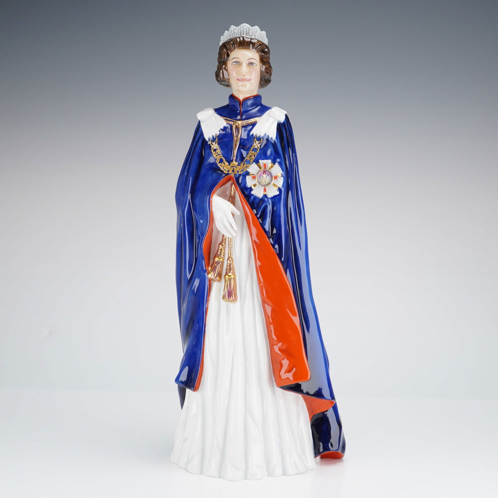 Royal Doulton Figurine Queen Elizabeth II HN2878: A glazed bone china figurine by Royal Doulton, depicting the Queen in full ceremonial attire, specifically the deep cobalt blue robes and chain of the Order of the Garter, accented with gold-colored d