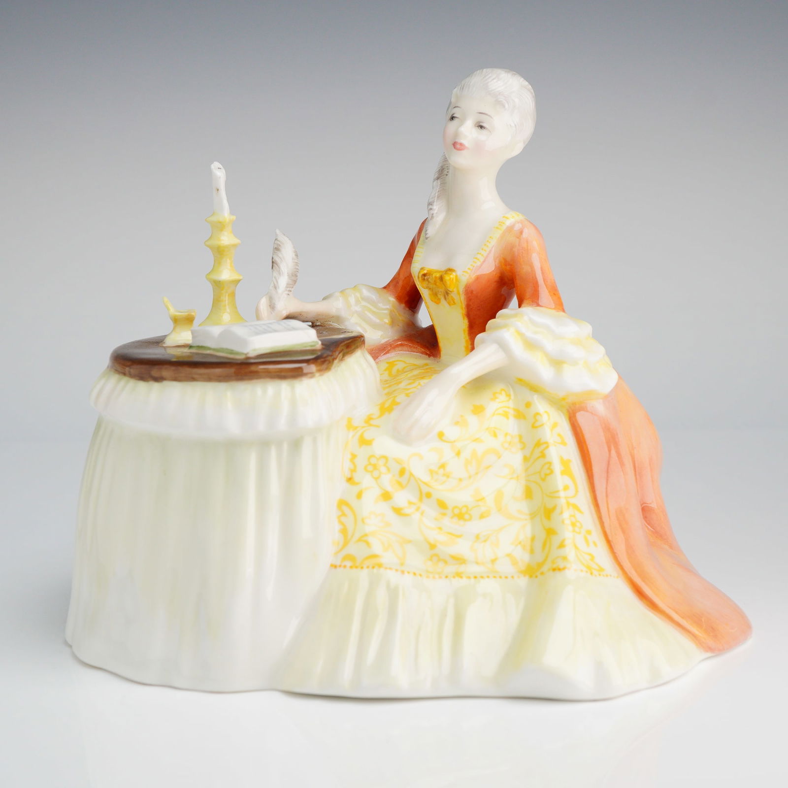 Royal Doulton Figurine, Meditation HN 2330: A Royal Doulton figurine, depicting a woman in an orange, yellow, and white 18th-century dress seated next to a table with a candle and book, marked underneath COPR 1970 DOULTON & CO LIMITED. Dimensio