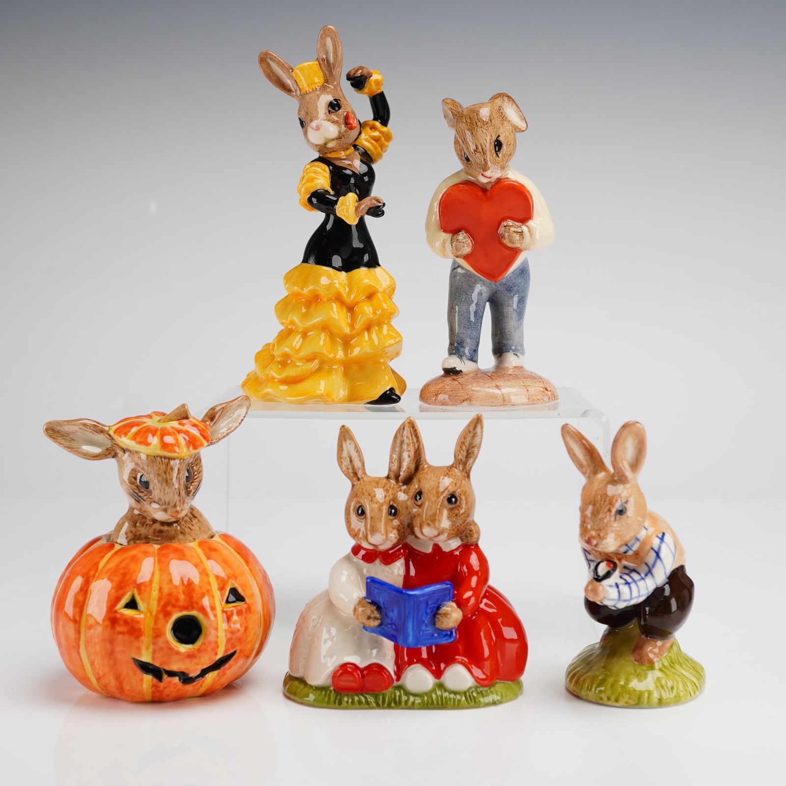 Collection of Five Royal Doulton Bunnykins Figurines Tom Halloween Heart: This collection of five Royal Doulton Bunnykins ceramic figurines consists of hand-painted pieces with glossy glaze finishes. The group includes Tom DB72, copyright 1988, Halloween DB132, copyright 19