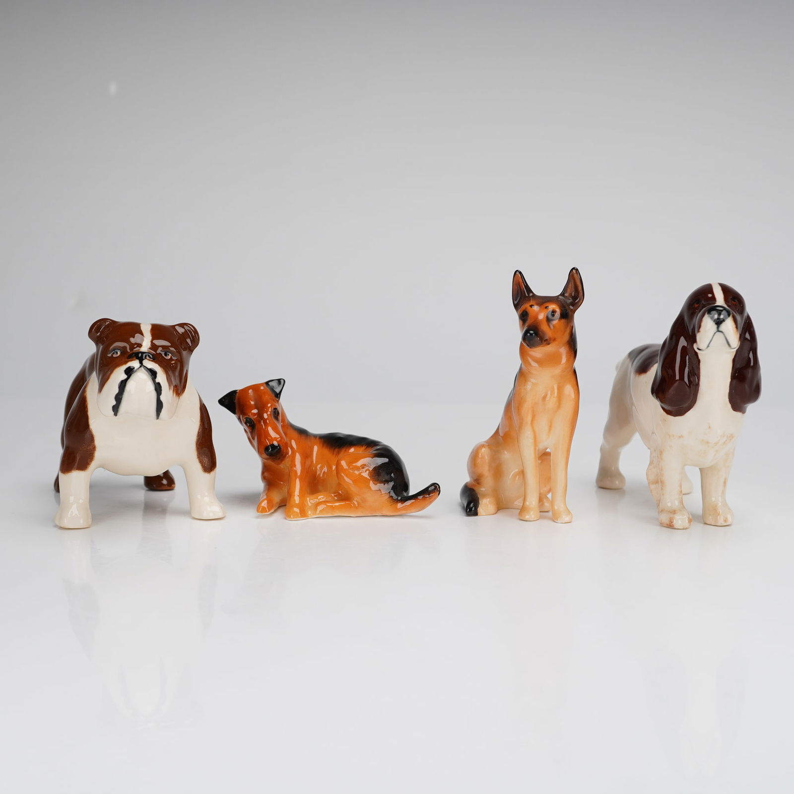 4pc Royal Doulton Bone China & Beswick Dog Figurines: A collection of 4pc Royal Doulton bone china and Beswick dog figurines, featuring various breeds including a Bulldog, a Terrier, a German Shepherd, and a Spaniel. Each piece is modeled in a realistic