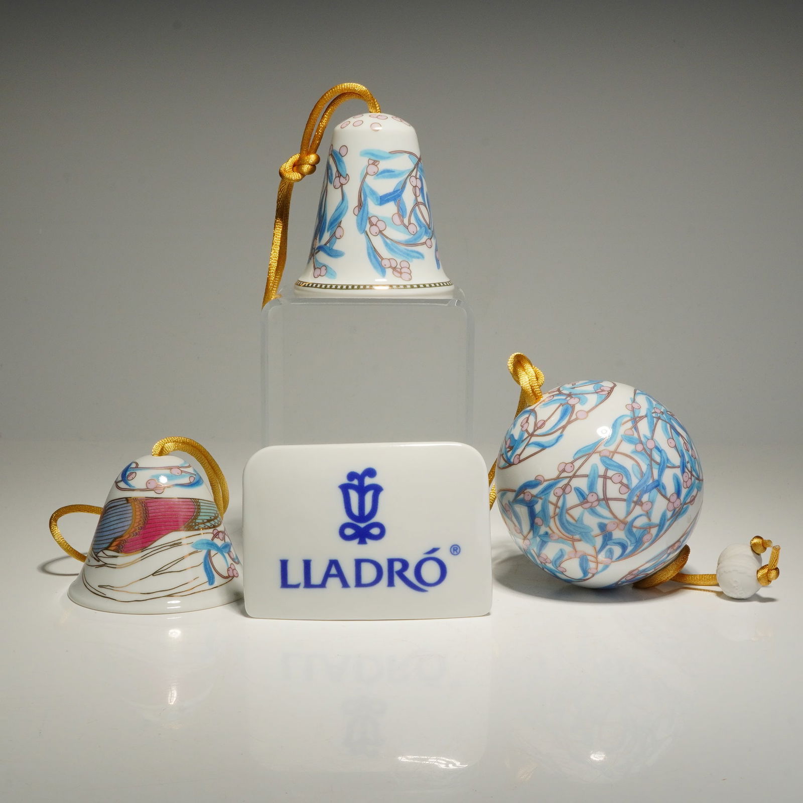 4pc Lladro Porcelain Christmas Ornaments and Plaque: A collection of Lladro porcelain Christmas ornaments and accessories, including one round ornament, two bell ornaments, and a branded porcelain name plaque. Angelic Melody Bell (1008078) depicts a
