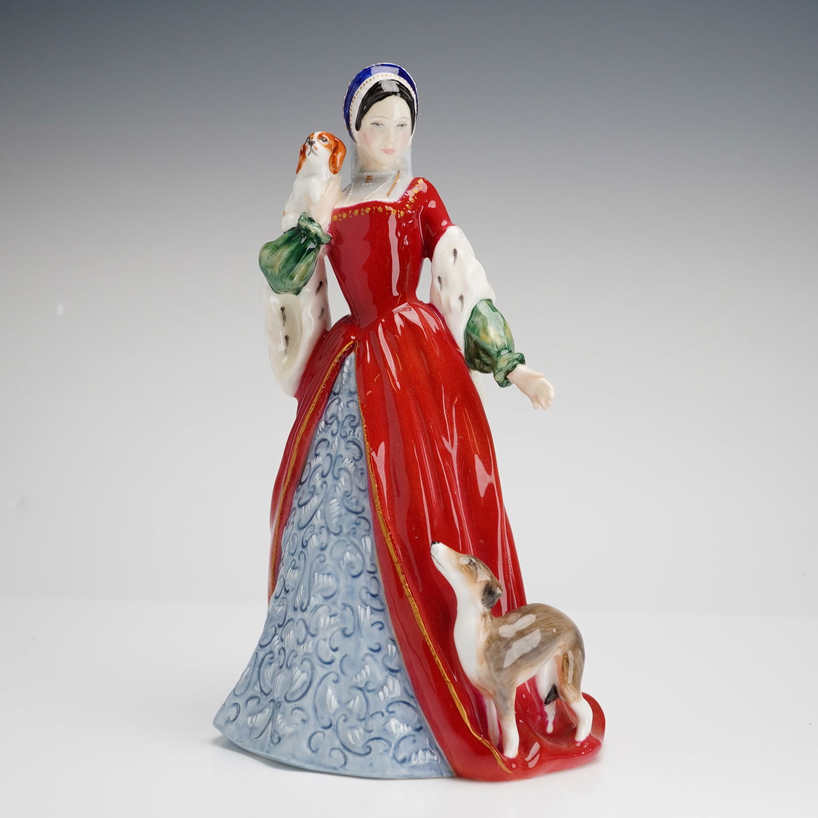Royal Doulton Figurine Anne Boleyn HN3232: Royal Doulton Anne Boleyn HN3232. This glazed porcelain figurine depicts the historical figure in a Tudor-style ensemble featuring a red gown with ermine-trimmed sleeves, a blue patterned underskirt,