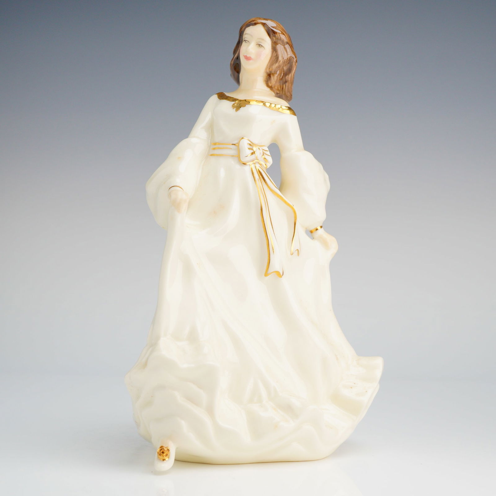 Royal Doulton Figurine, Free Spirit HN3728: The piece depicts a female figure in a flowing, cream-colored gown with voluminous sleeves. Decoration includes gold gilt detailing applied to the neckline, ribbon sash, and shoe accents. The undersid