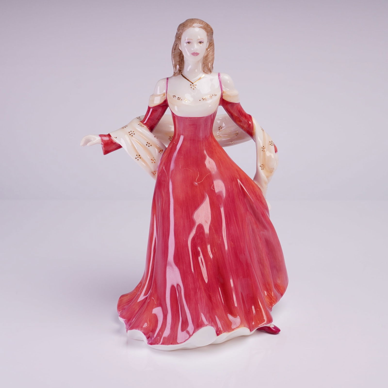 Royal Doulton Prestige Figure of the Year 2005, Lady Sarah Jane HN4793: The figure depicts a standing woman in a romantic style, wearing a long, high-gloss red gown with a cream-colored shawl draped over her shoulders. The shawl is decorated with applied gold dot accents.