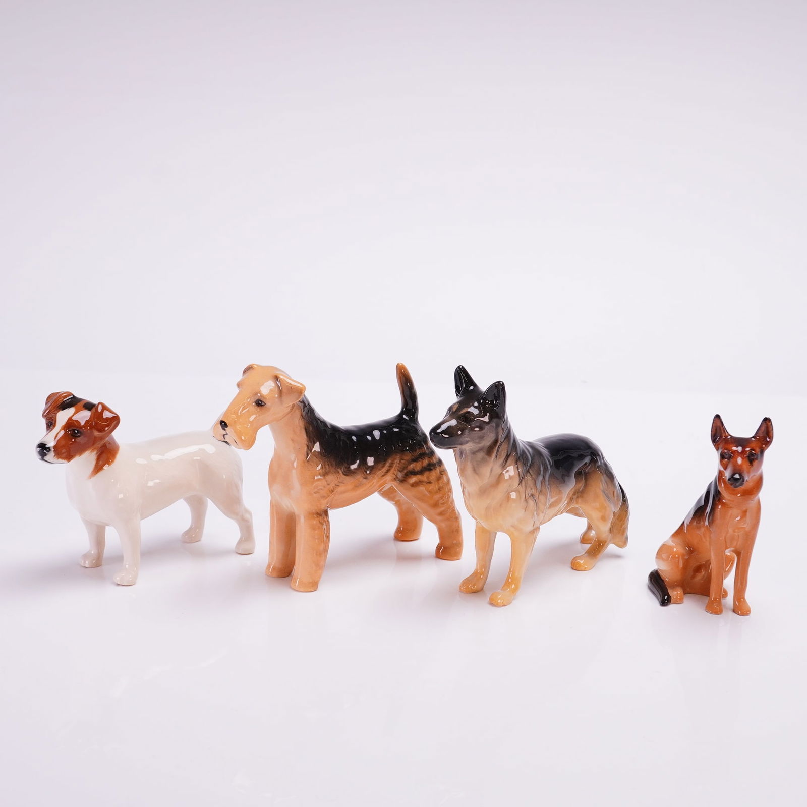Collection of Four Beswick and Royal Doulton Dog Figurines: The group features a variety of breeds including a Jack Russell Terrier, an Airedale Terrier, and two German Shepherds. The Royal Doulton figure is a seated Alsatian marked K13 on the underside. The r
