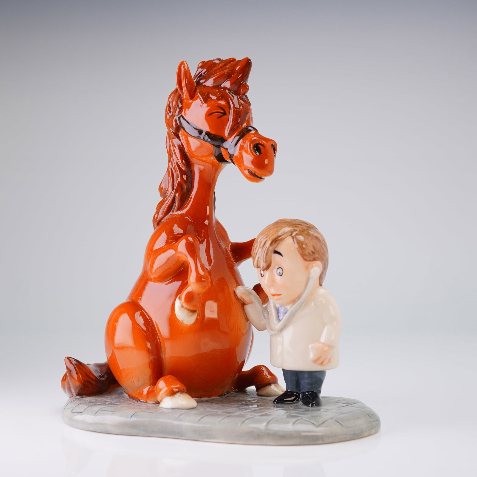 Royal Doulton Thelwell Pony Figurine, Detecting Ailments NT8: The piece depicts a humorous scene featuring a small veterinarian in a white coat applying a stethoscope to the chest of a large, reddish-brown horse (Thelwell pony) seated on its haunches. The figure