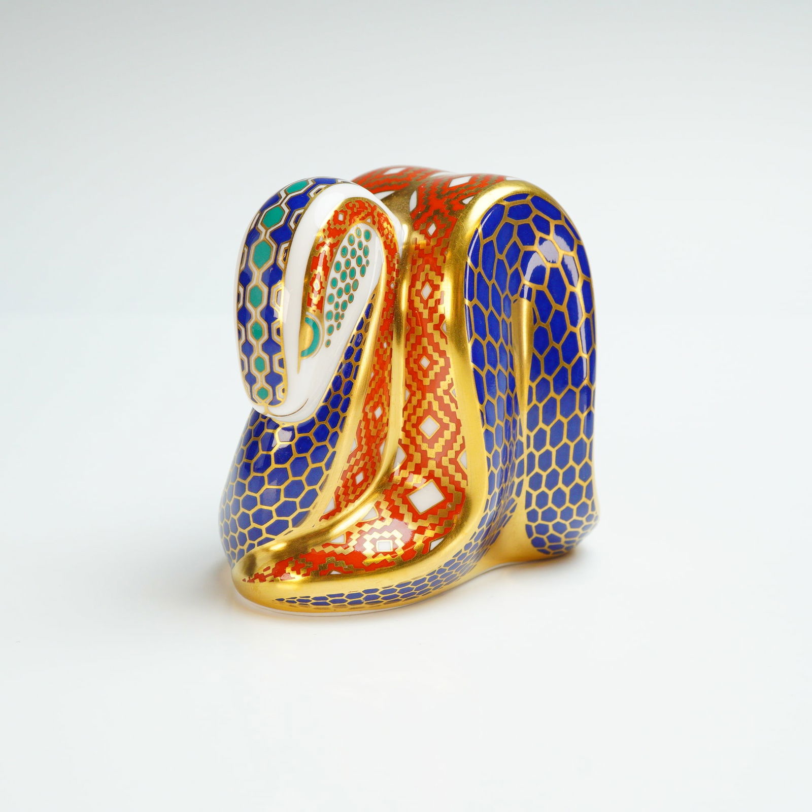 Royal Crown Derby Paperweight, Snake: The piece is decorated in an Imari-style pattern featuring cobalt blue, iron red, and white with extensive gold gilding. The decoration includes a honeycomb scale motif and geometric zigzags. The base