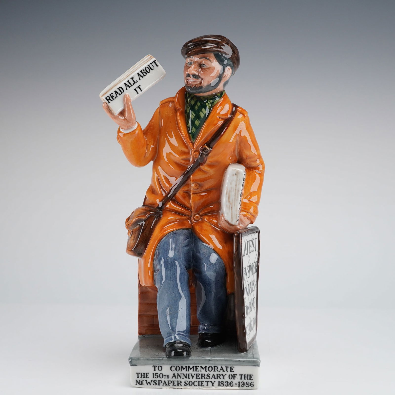 Royal Doulton Figurine, The Newsvendor HN 2891: The figure depicts a seated man, modeled by William T. Harper, wearing an orange trench coat, blue trousers, and a brown cap, holding a newspaper aloft inscribed READ ALL ABOUT IT. The figure is leani
