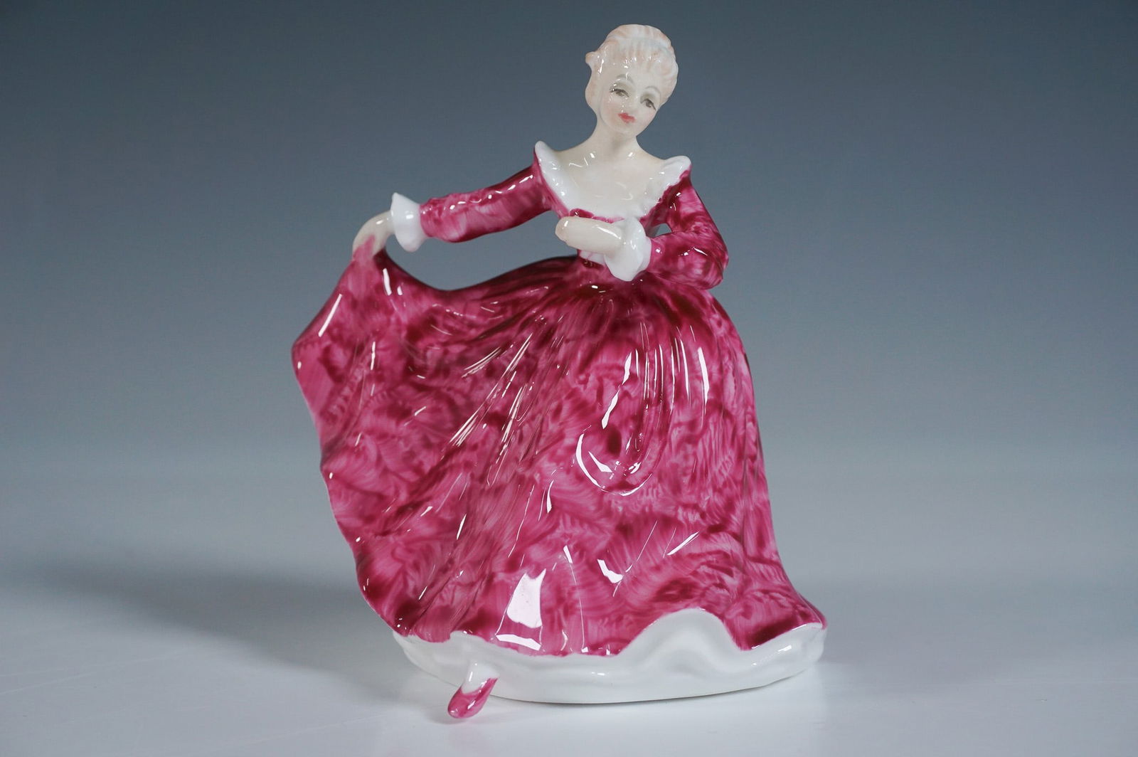 Royal Doulton Mini Figurine, Kirsty HN3213: This delightful and charming piece features a young lady in a swirling pink marbled gown with white accents, holding her dress elegantly. The figurine showcases fine craftsmanship with intricate detai