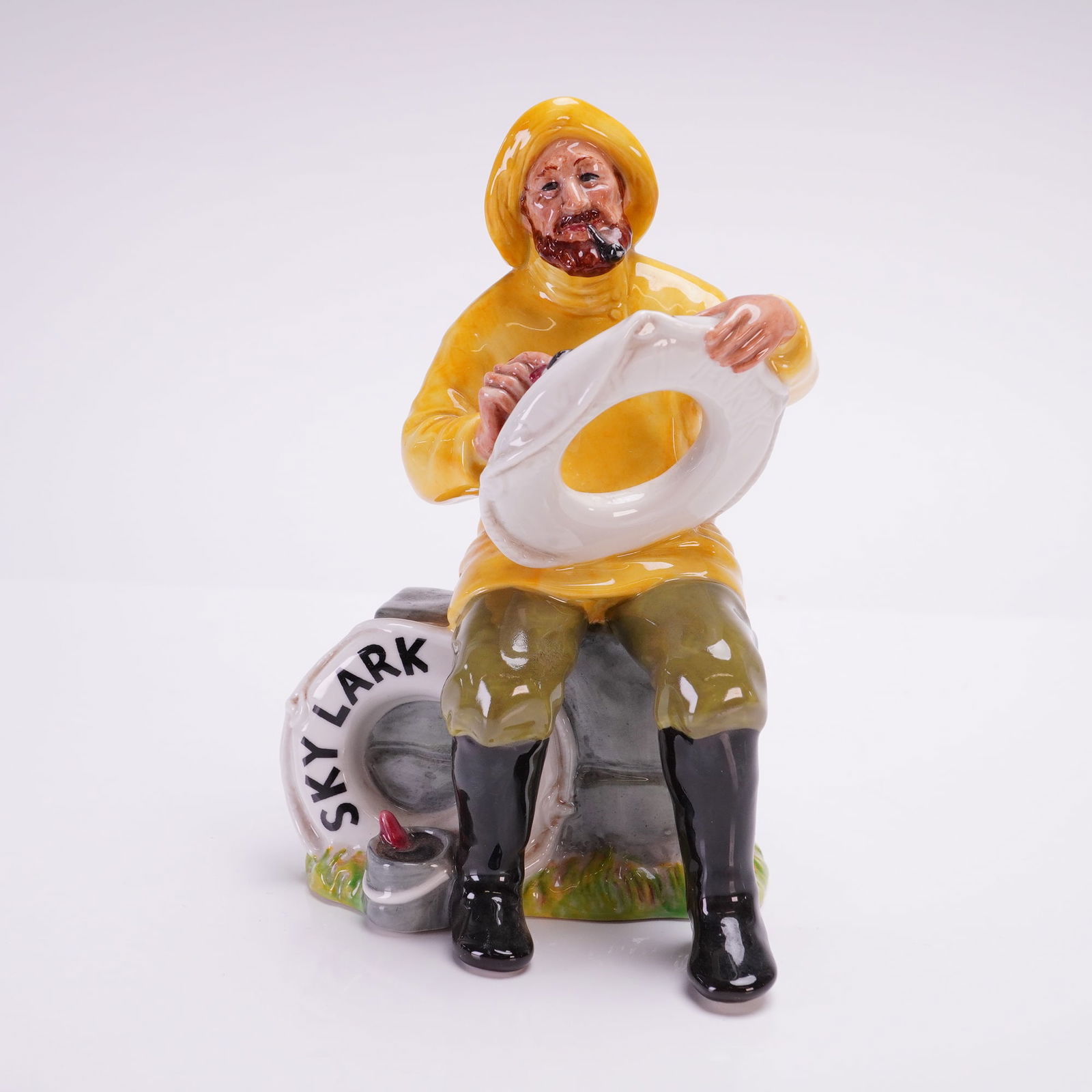 Royal Doulton Figurine, The Boatman (Skylark) HN2417: This piece was designed by Mary Nicoll and is dated 1970. The figure depicts a seated, bearded mariner wearing a yellow sou'wester hat and slicker over green trousers and black boots. He is portrayed