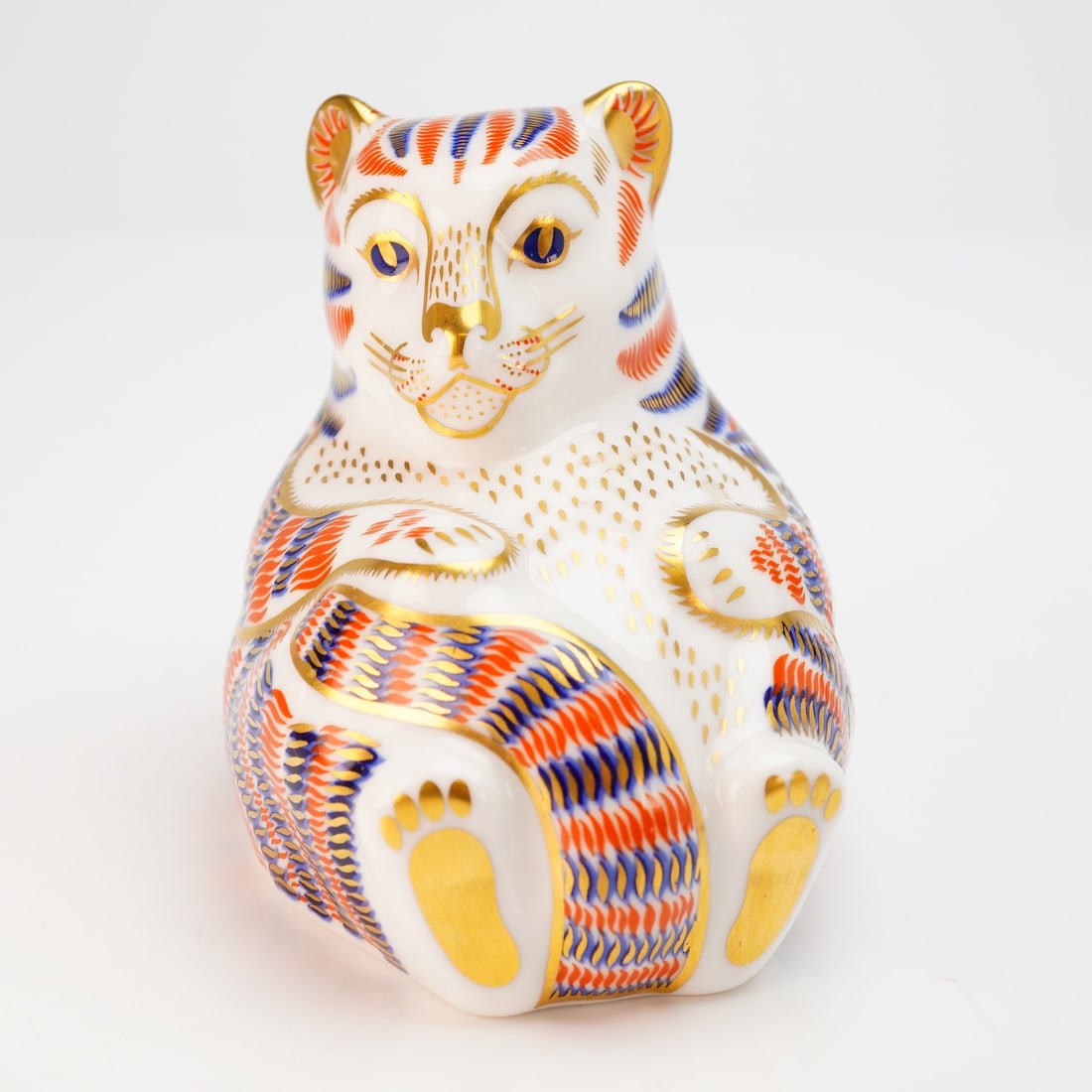 Royal Crown Derby Tiger Cub Paperweight with Box: A Royal Crown Derby bone china paperweight in the form of a seated Bengal tiger cub, decorated in a traditional Imari palette of orange and cobalt blue with extensive gilded highlights throughout. The