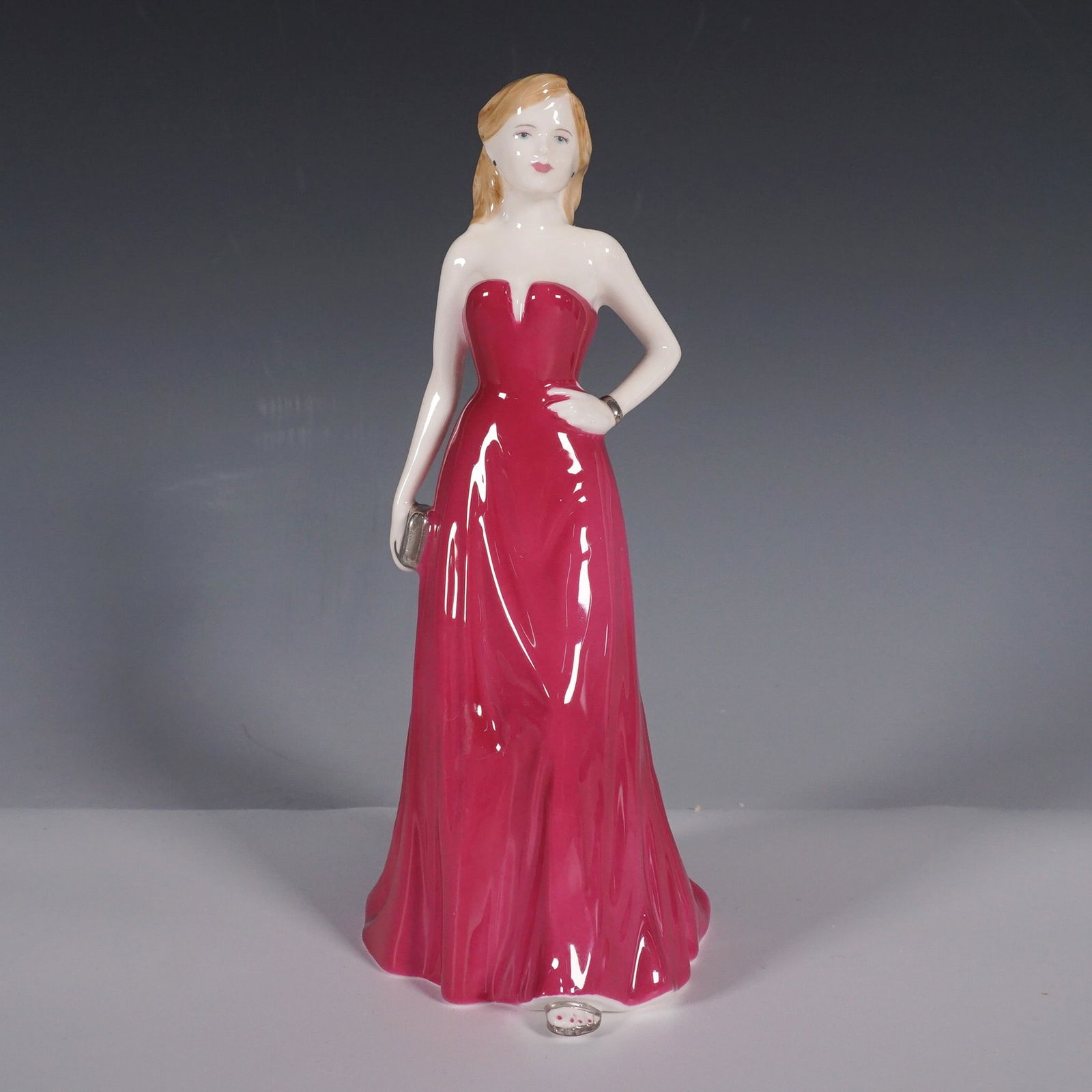 Royal Doulton Figurine Abigail HN4664: This elegant Royal Doulton figurine, titled Abigail (HN4664), features a graceful young woman in a flowing red gown, holding a silver clutch. Designed by Nada M. Pedley and issued in 2004, this piece
