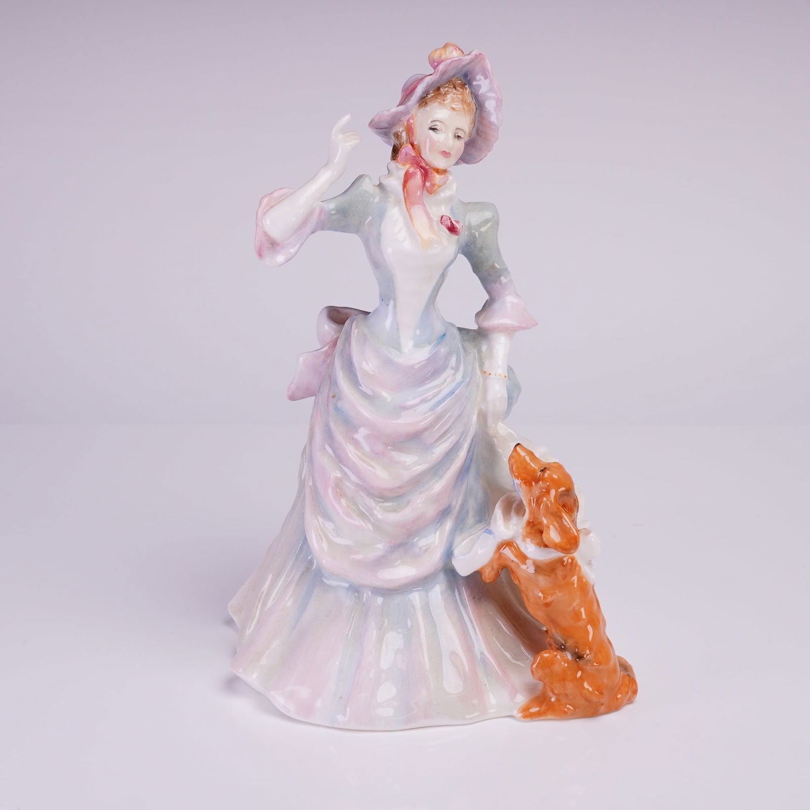 Royal Doulton Figurine, Loyal Friend HN3358: The figurine depicts a finely dressed woman in a historical style gown and bonnet, interacting with a reddish-brown spaniel-type dog sitting upright beside her. The piece is decorated in a polychrome