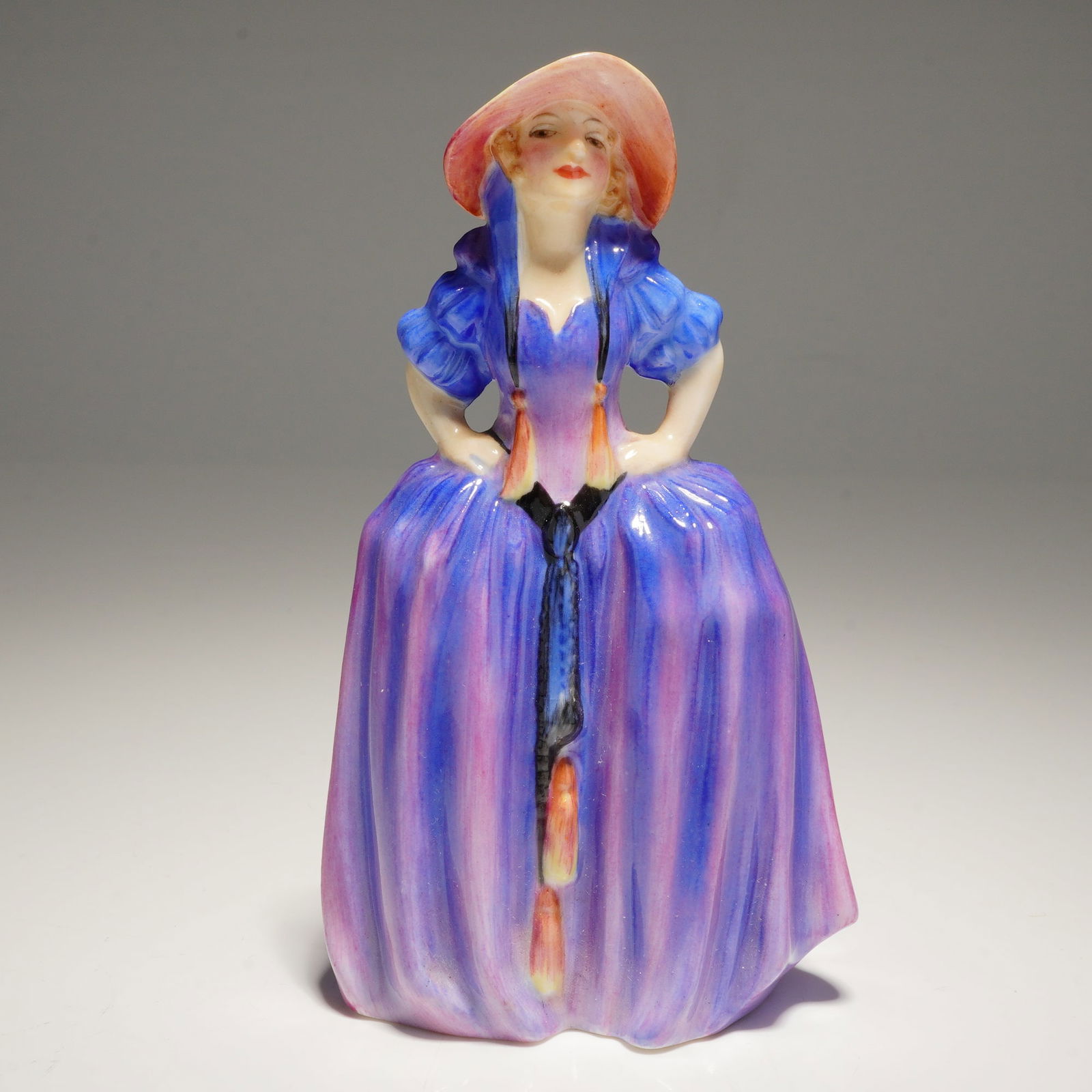 Royal Doulton Miniature Figurine Patricia M28: A single Patricia M28 Royal Doulton Figurine, depicting a woman in a voluminous purple, blue, and pink dress and a broad-brimmed hat, bearing the base marks MADE IN ROYAL DOULTON ENGLAND and R No 7554