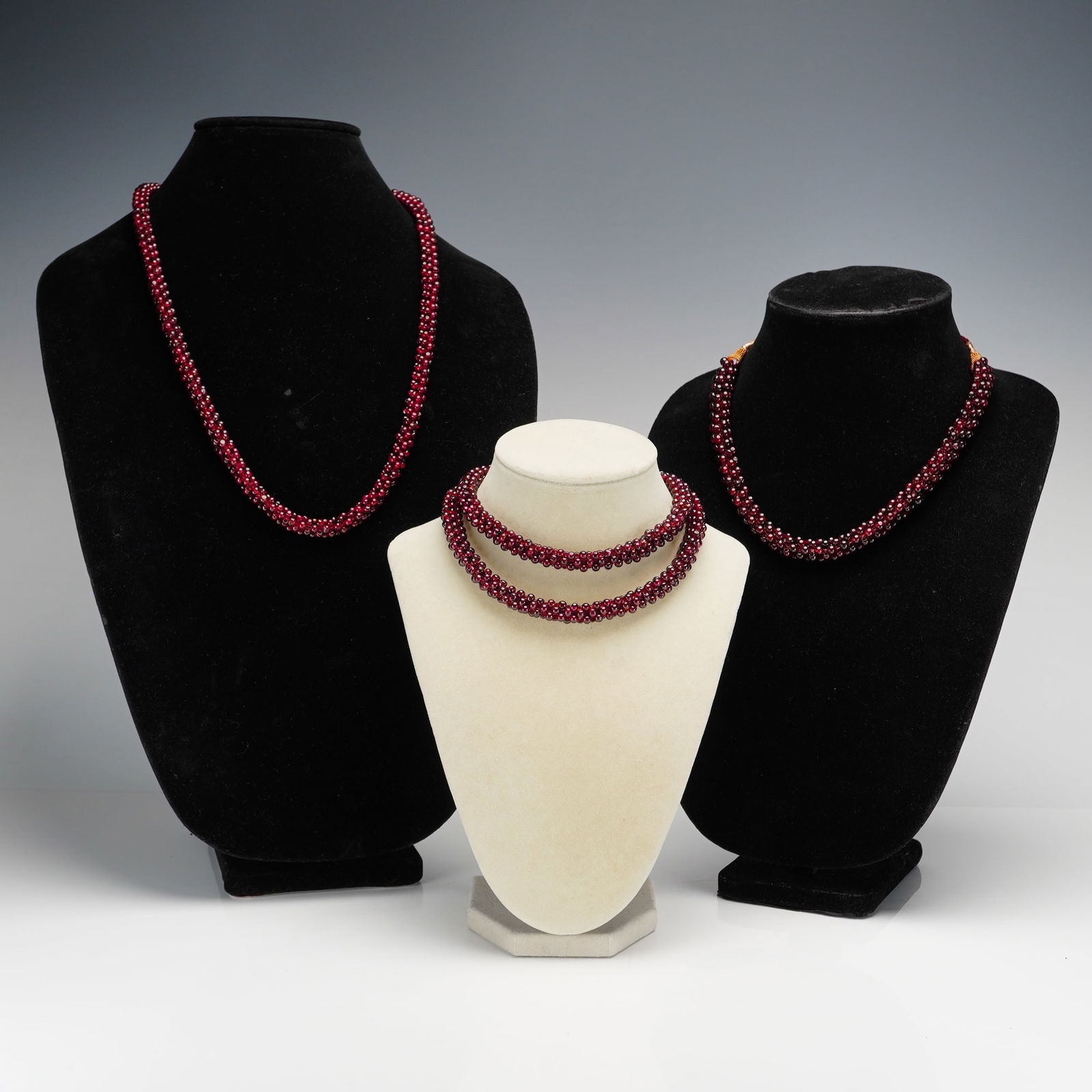 3pc Red Garnet Woven Rope Cluster Bead Necklaces: A trio of necklaces composed of small, polished, deep red round garnet beads arranged in a twisted rope-style torsade design. One necklace features gold-toned, wire-wrapped conical caps that