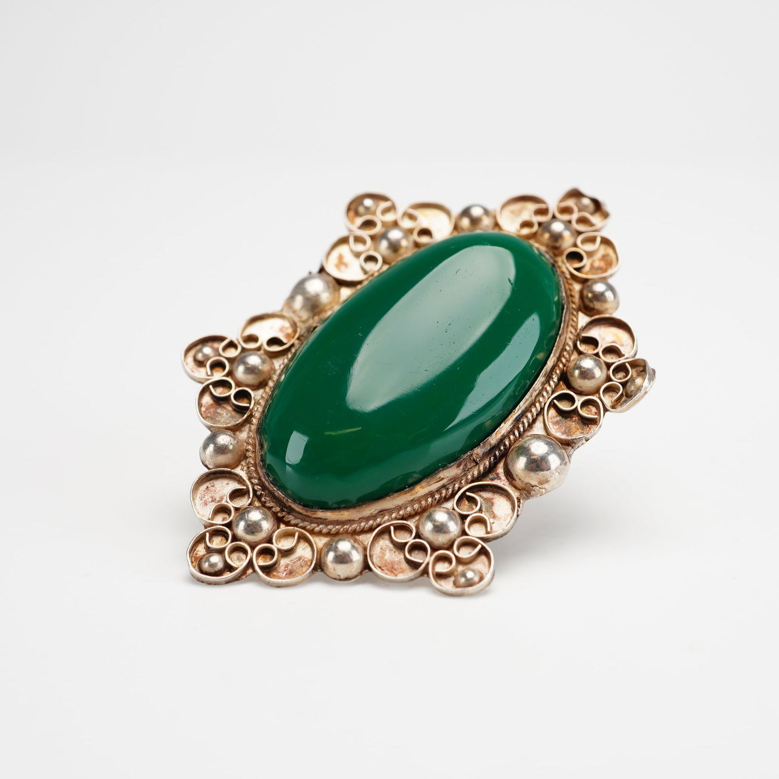 Mexican 925 Sterling Silver Green Oval Stone Ring: This artisanal Mexican jewelry piece is a 925 sterling silver ring with a large green oval cabochon. The stone is secured in a bezel setting surrounded by an ornate sterling silver frame featuring
