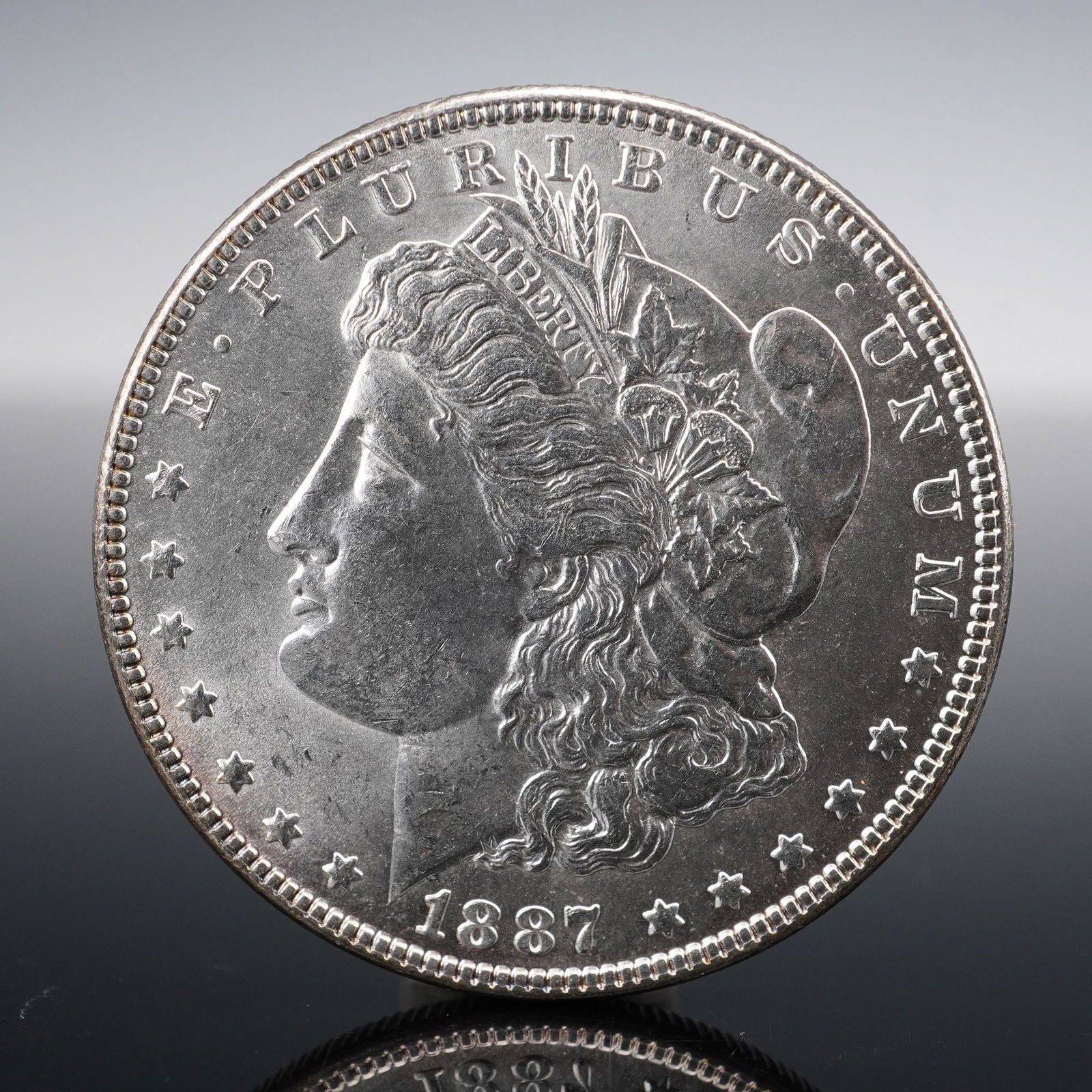 1887 Morgan Silver Dollar: Minted in 1887, this Morgan Silver Dollar was struck in the traditional alloy of 90% silver. The obverse features George T. Morgan's celebrated design of Liberty in profile, wearing a Phrygian cap ado