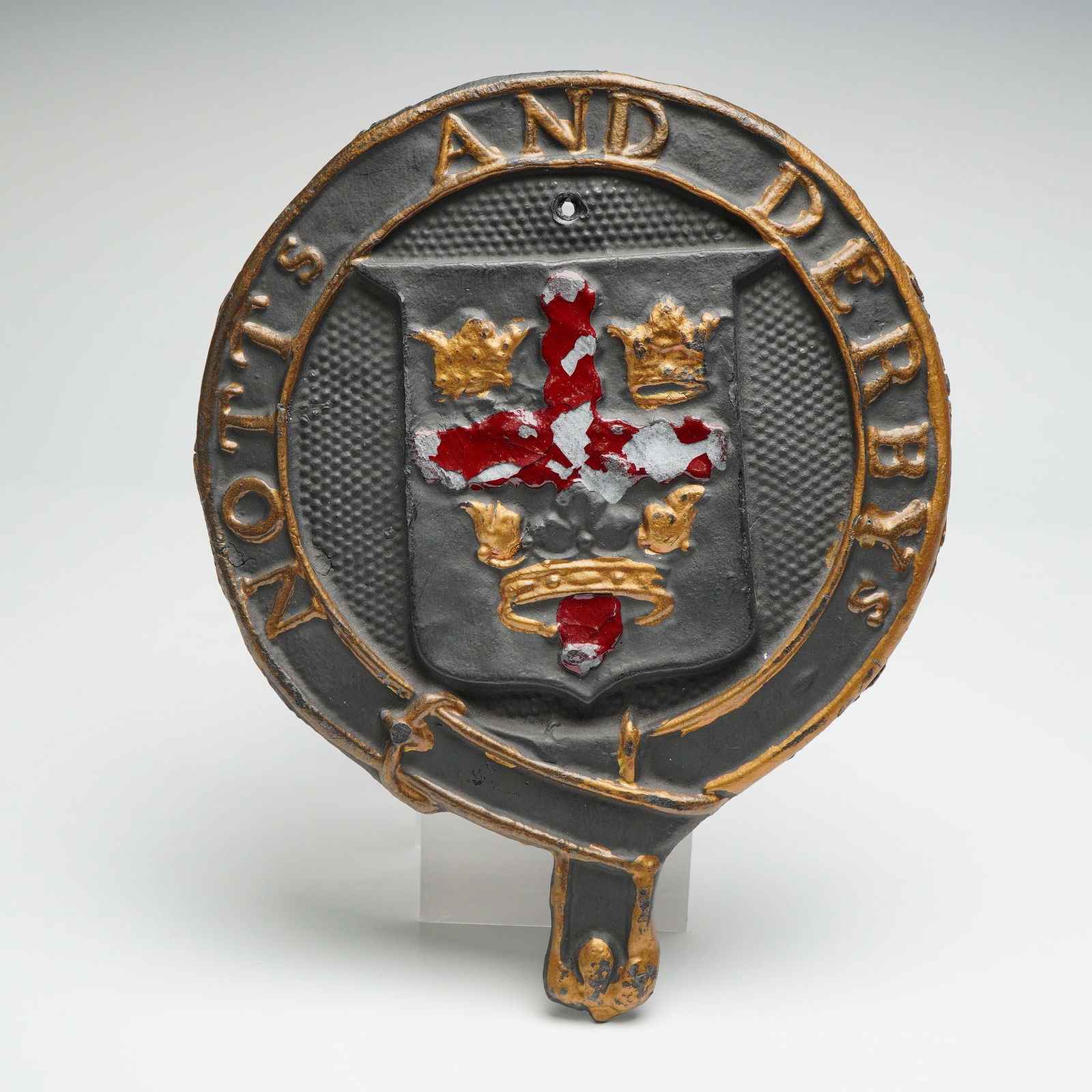 Notts and Derbys Cast Metal Crest Wall Plaque: This cast metal plaque features a flat section discoid form shaped as a garter with raised lettering for Notts and Derbys surrounding a central shield bearing the red cross and crown motif associated