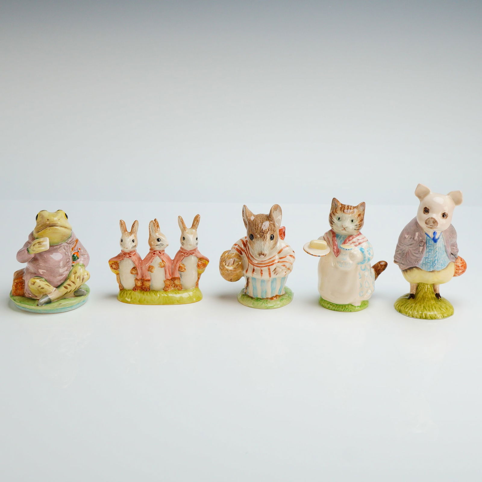 5pc Royal Albert Beatrix Potter Ceramic Figurines: A set of five glazed ceramic figurines produced by Royal Albert, England, depicting characters from the stories of Beatrix Potter. The collection includes figures of Jeremy Fisher, Flopsy, Mopsy and C