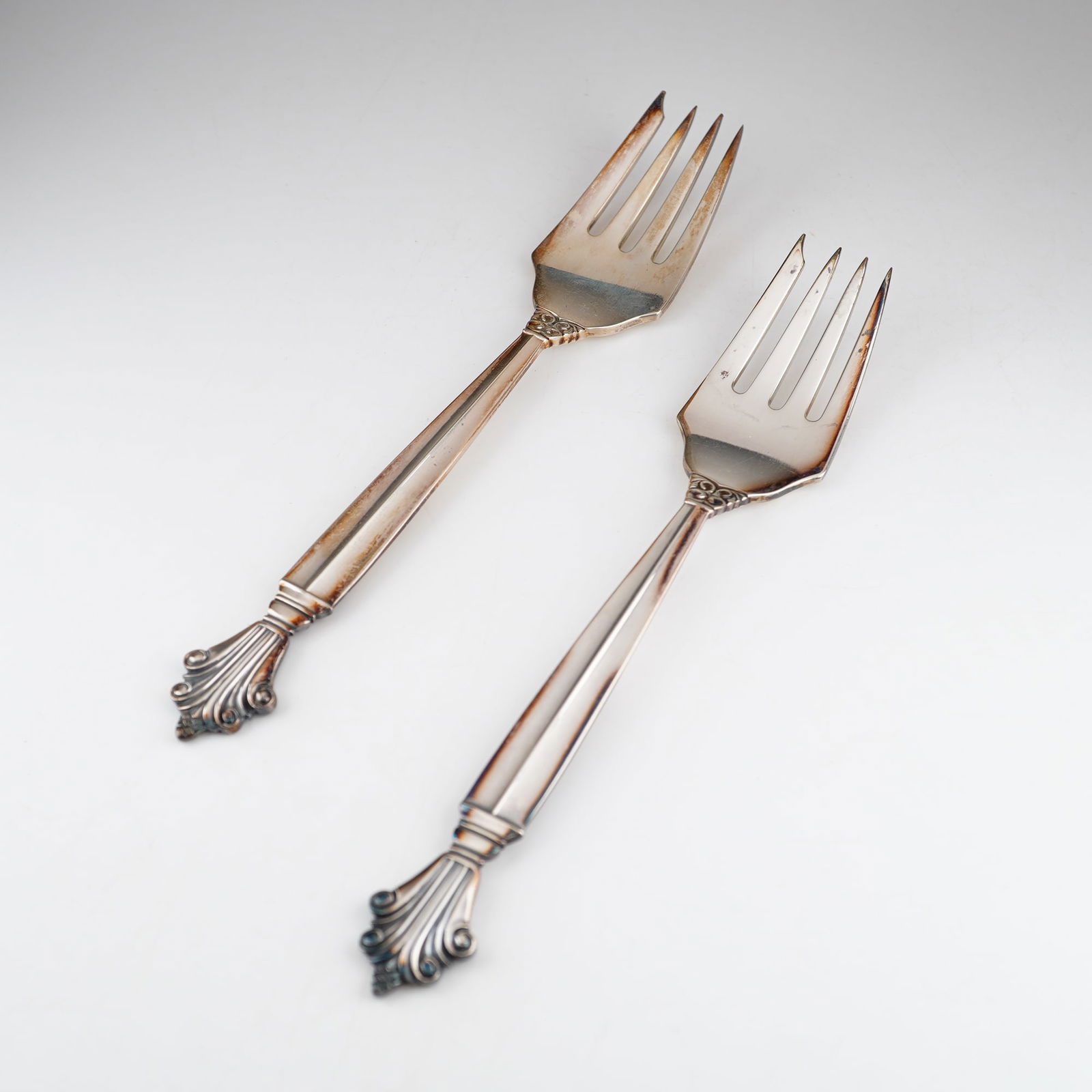 2pc Georg Jensen Sterling Silver Salad Forks, Acanthus: A pair of sterling silver pastry forks in the Acanthus pattern, designed by Johan Rohde for Georg Jensen. Each fork features a tapered, faceted handle terminating in a decorative flared end with