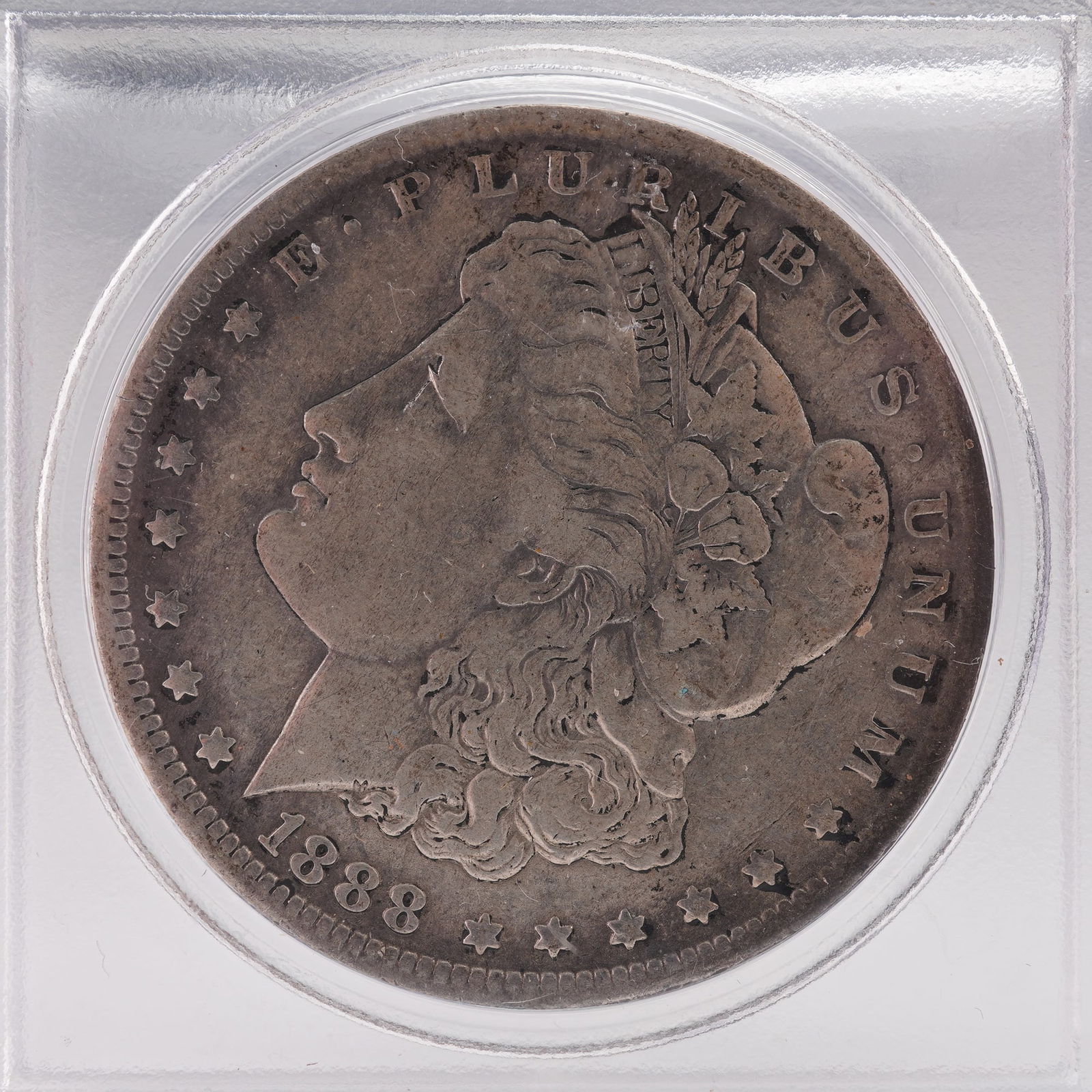 1888 Morgan Silver Dollar: This 1888 Morgan Silver Dollar, created by George T. Morgan, comes housed in a protective case. The obverse portrays Liberty wearing a Phrygian cap adorned with wheat and cotton, surrounded by stars