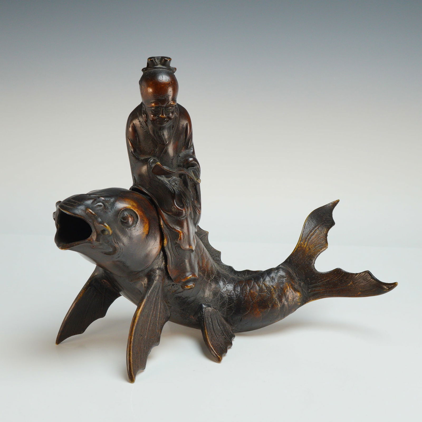 Asian Bronze Cast Taoist Qin Gao Riding a Carp Incense Burner: A two-piece Asian cast bronze incense burner depicting the Taoist immortal Qin Gao riding a carp. The set is constructed of hollow-cast bronze with a dark brown patinated finish and faint traces of
