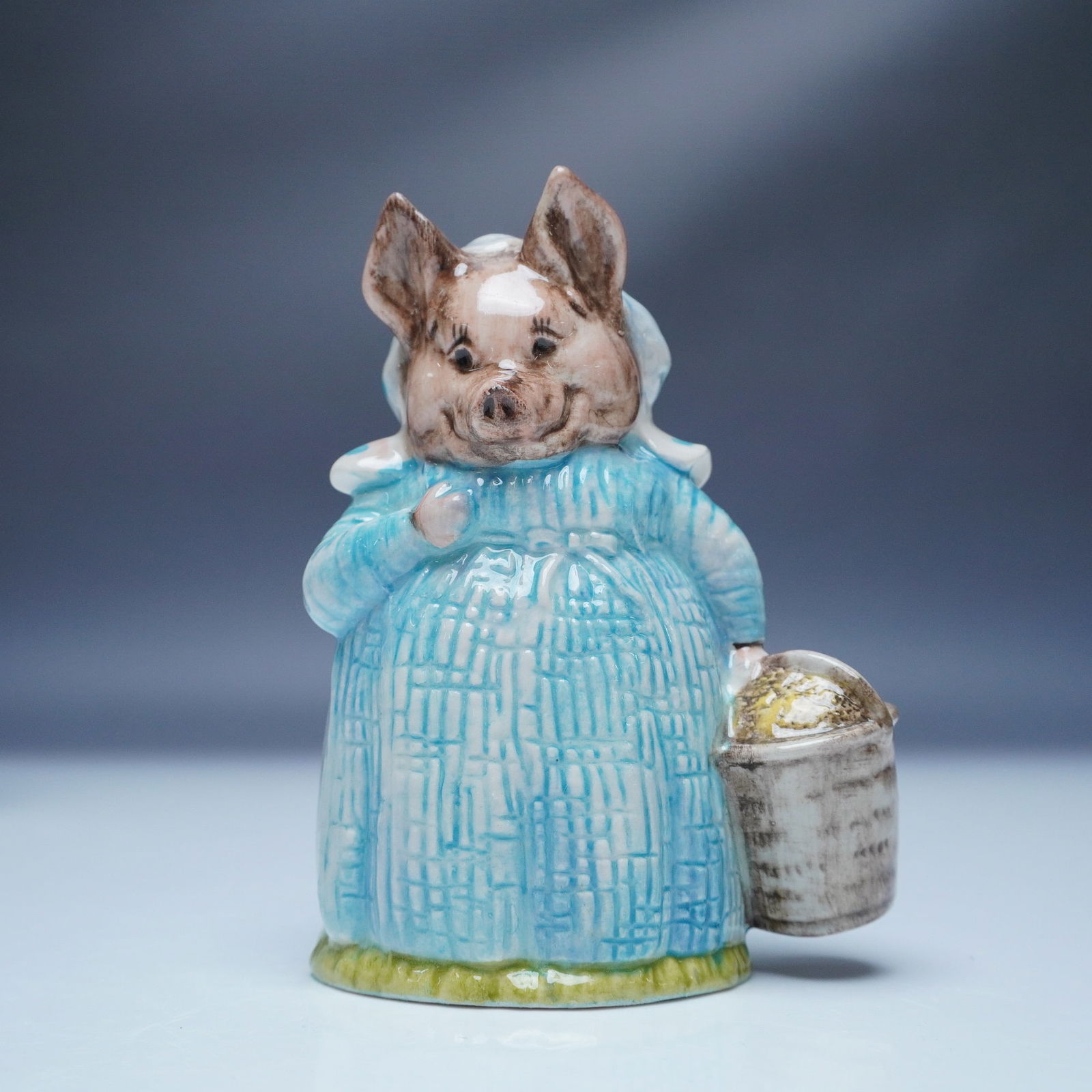 Royal Albert Beatrix Potter Figurine, Aunt Pettitoes: This Royal Albert figurine brings to life Aunt Pettitoes, the endearing pig character from Beatrix Potter's classic tales. Dressed in a textured blue gown with a matching bonnet, she holds a bucket, r