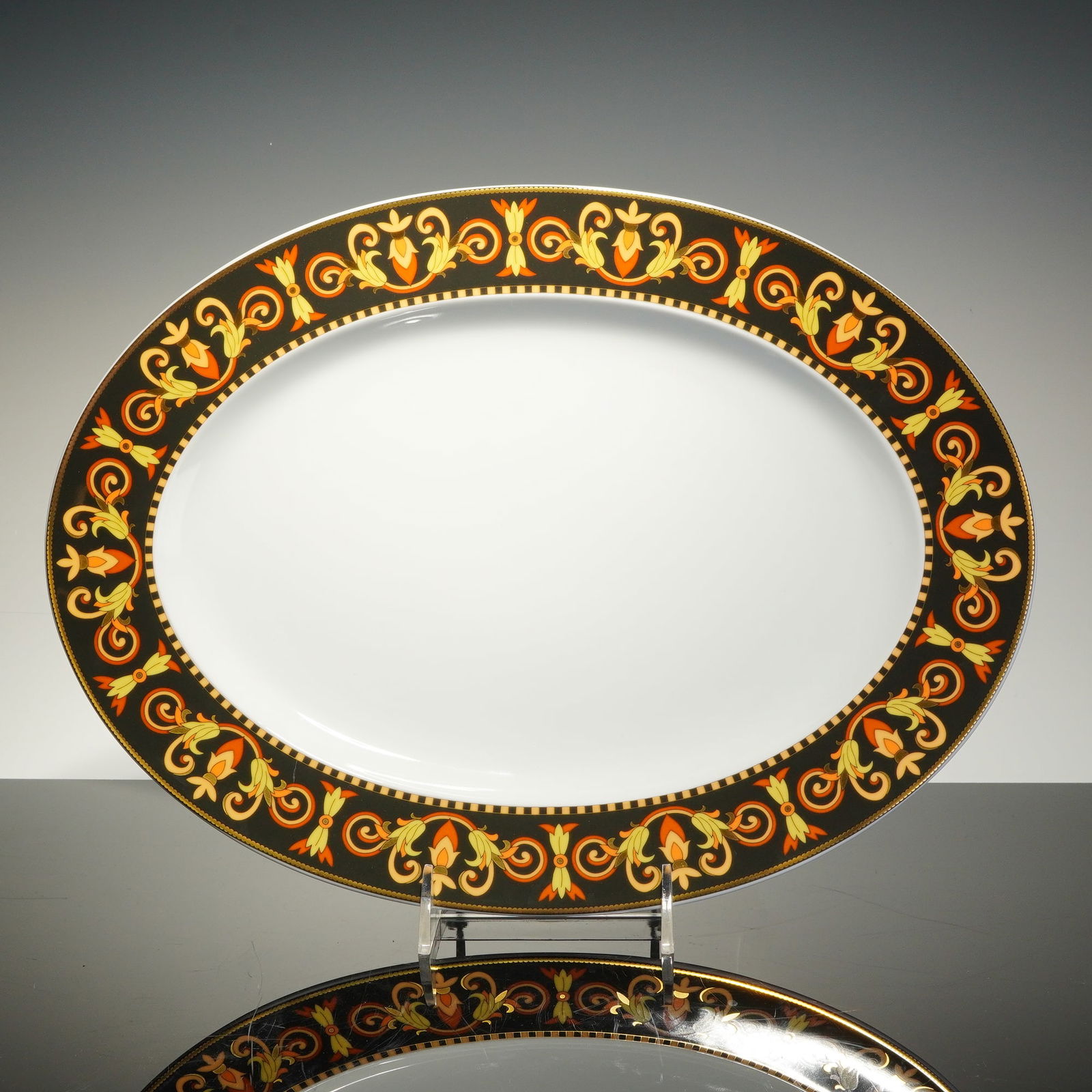 Rosenthal Versace Porcelain Oval Platter, Barocco: The oval form features a wide black border decorated with a repeating pattern of golden-yellow and orange acanthus leaf scrolls and stylized floral motifs in a neo-classical style. The decorative