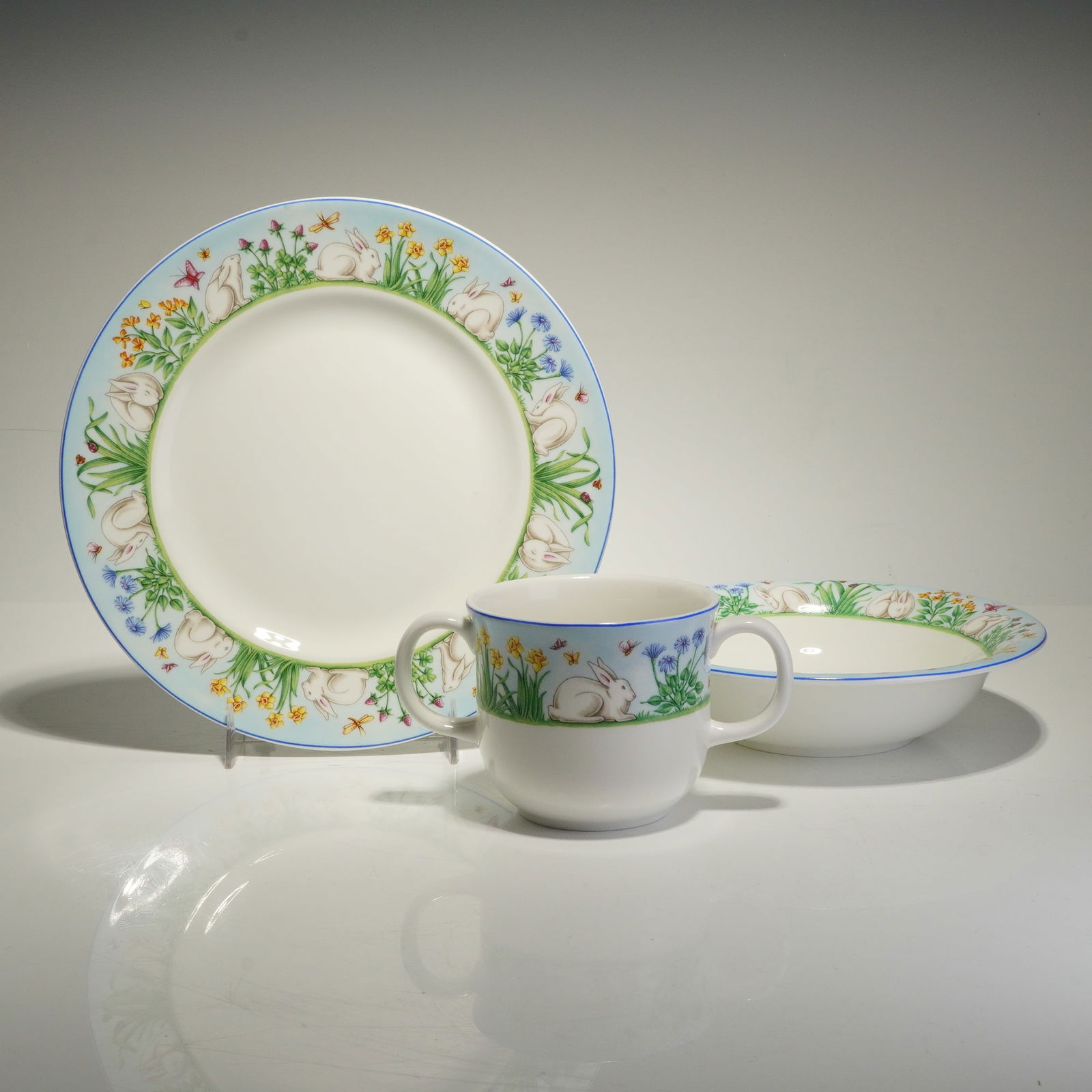 Tiffany & Co. England 3 Piece Child's Dinnerware Set, Tiffany Meadows: A trio of Tiffany & Co. English made porcelain children's tableware pieces in the Tiffany Meadows pattern. The group consists of a plate, a bowl, and a double handled mug. Each item is decorated with