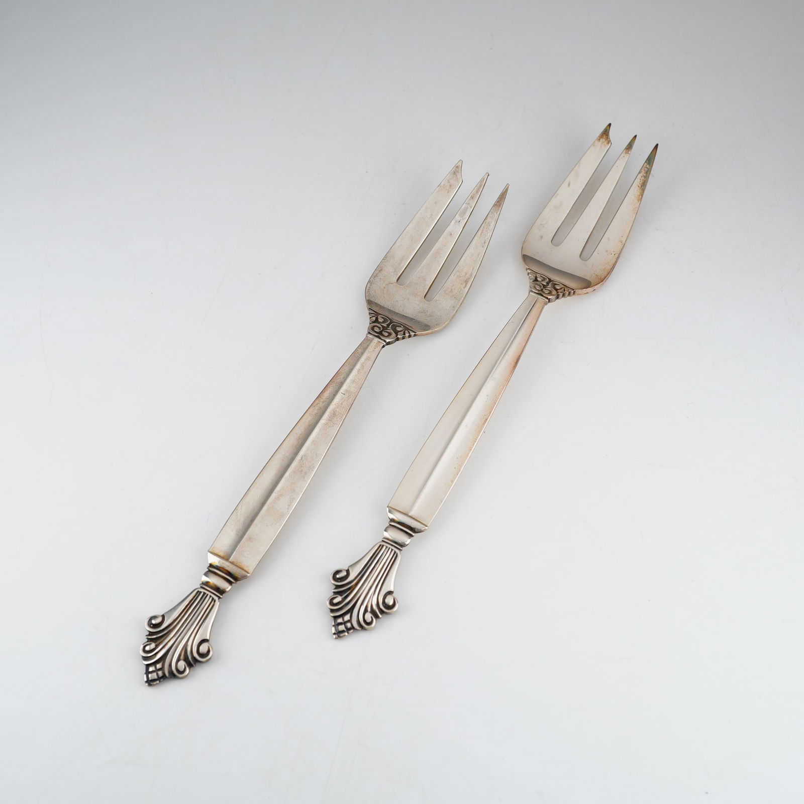 2pc Georg Jensen Sterling Silver Pastry Forks, Acanthus: A pair of sterling silver pastry forks in the Acanthus pattern by Georg Jensen, designed by Johan Rohde. Each fork is constructed with three wide tines and a tapered handle. The decorative elements