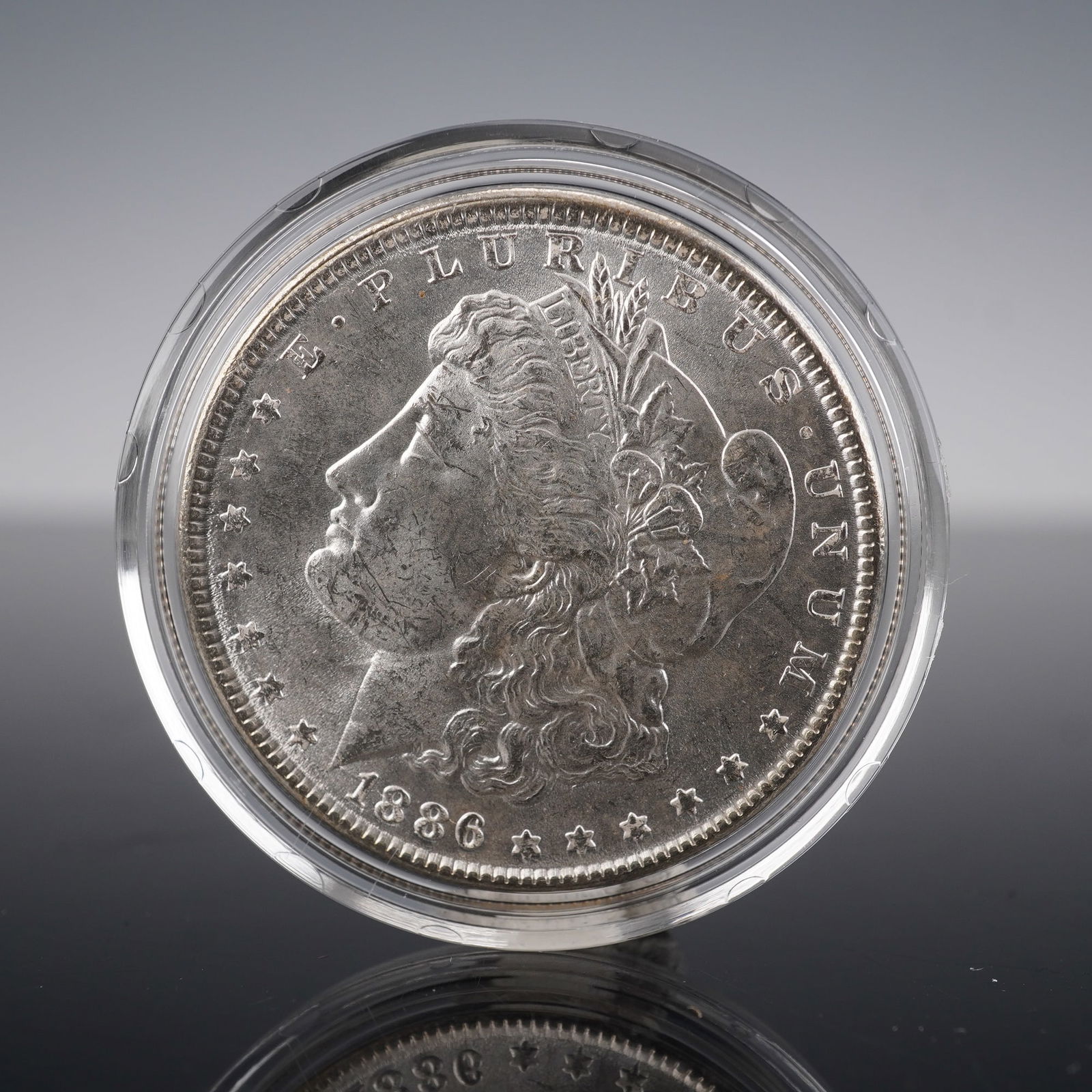 1886 Morgan Silver Dollar Coin: This 1886 Morgan Silver Dollar features two iconic designs. The obverse shows the Liberty head, facing left, with the inscription E ? PLURIBUS ? UNUM, LIBERTY, and the year 1886 below. The reverse
